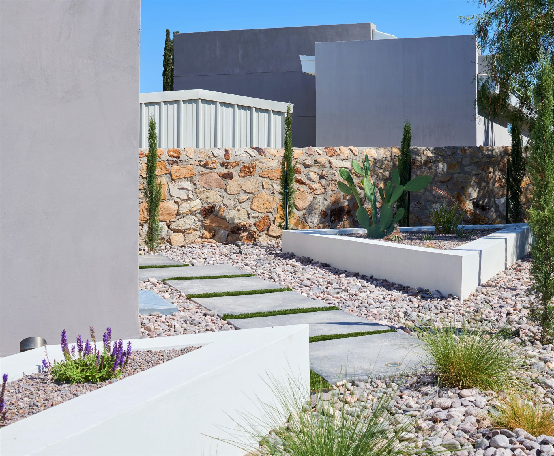 Concrete walkway with gravel, stone wall, and desert landscaping against modern architecture.