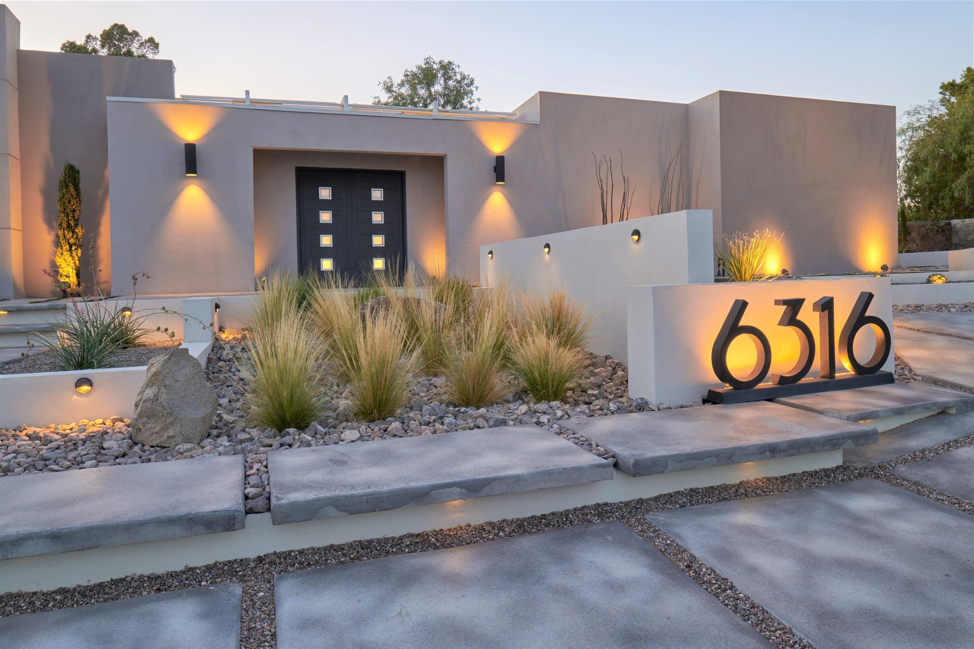 Modern home exterior with illuminated address numbers, walkways, and landscaping.