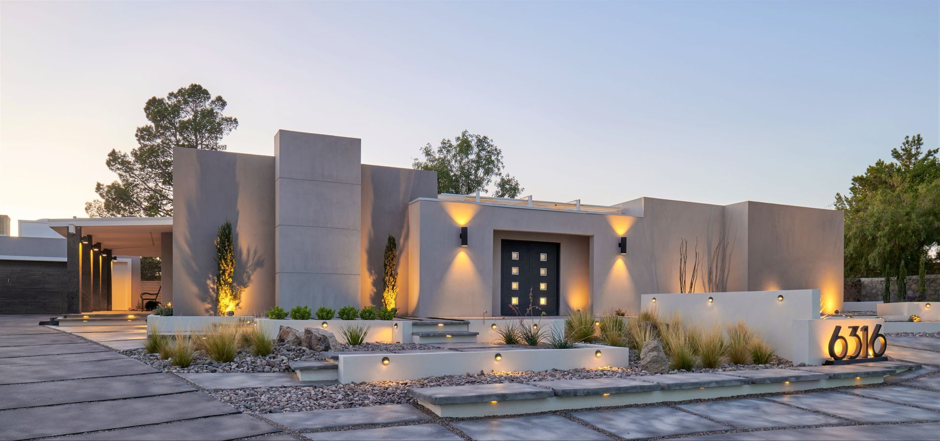 Modern house exterior with gray walls, lit entry, and landscaped front yard.