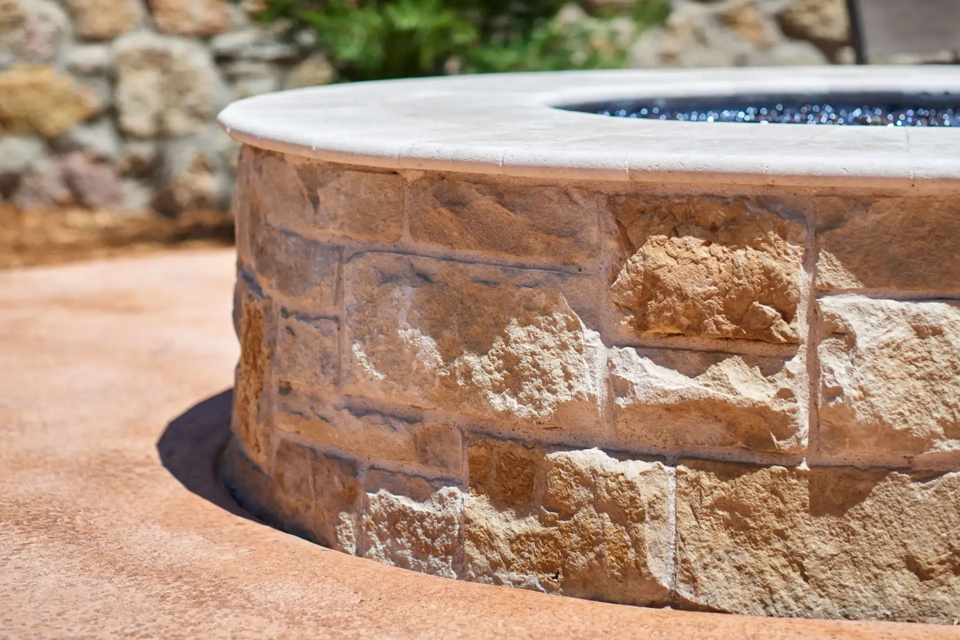 Stone fire pit with a light-colored concrete rim and a stone base, set in an outdoor area.