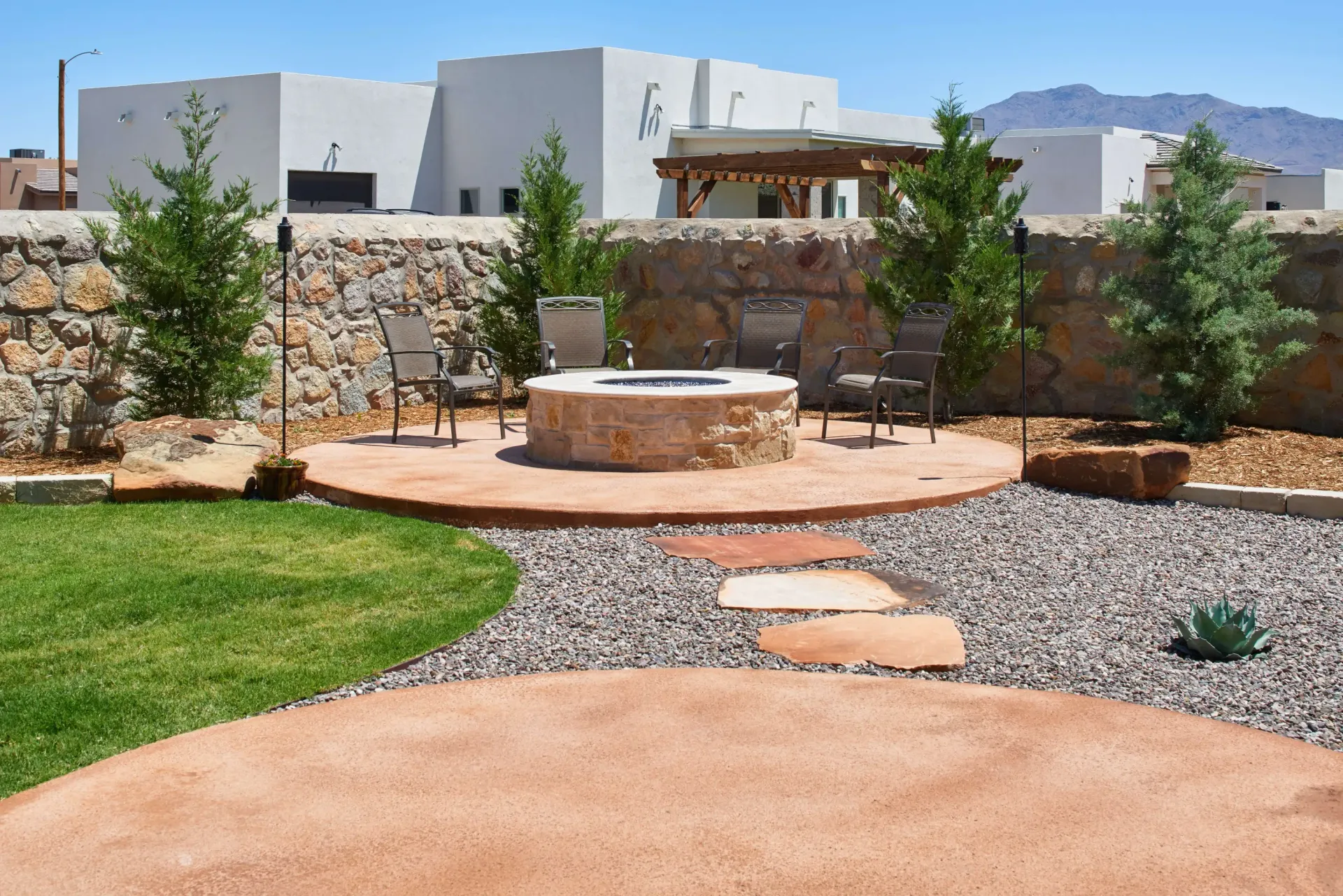 Backyard fire pit area with stone wall, chairs, and landscaped elements.