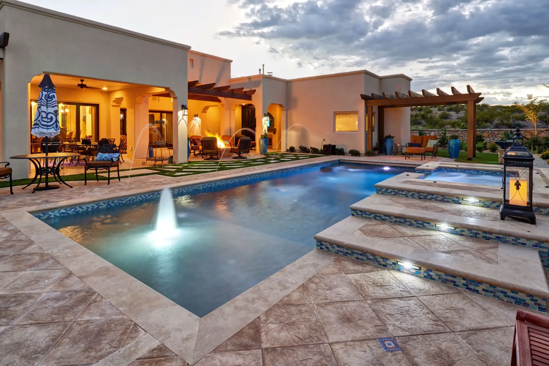 Poolside patio with pool, spa, and house at dusk.