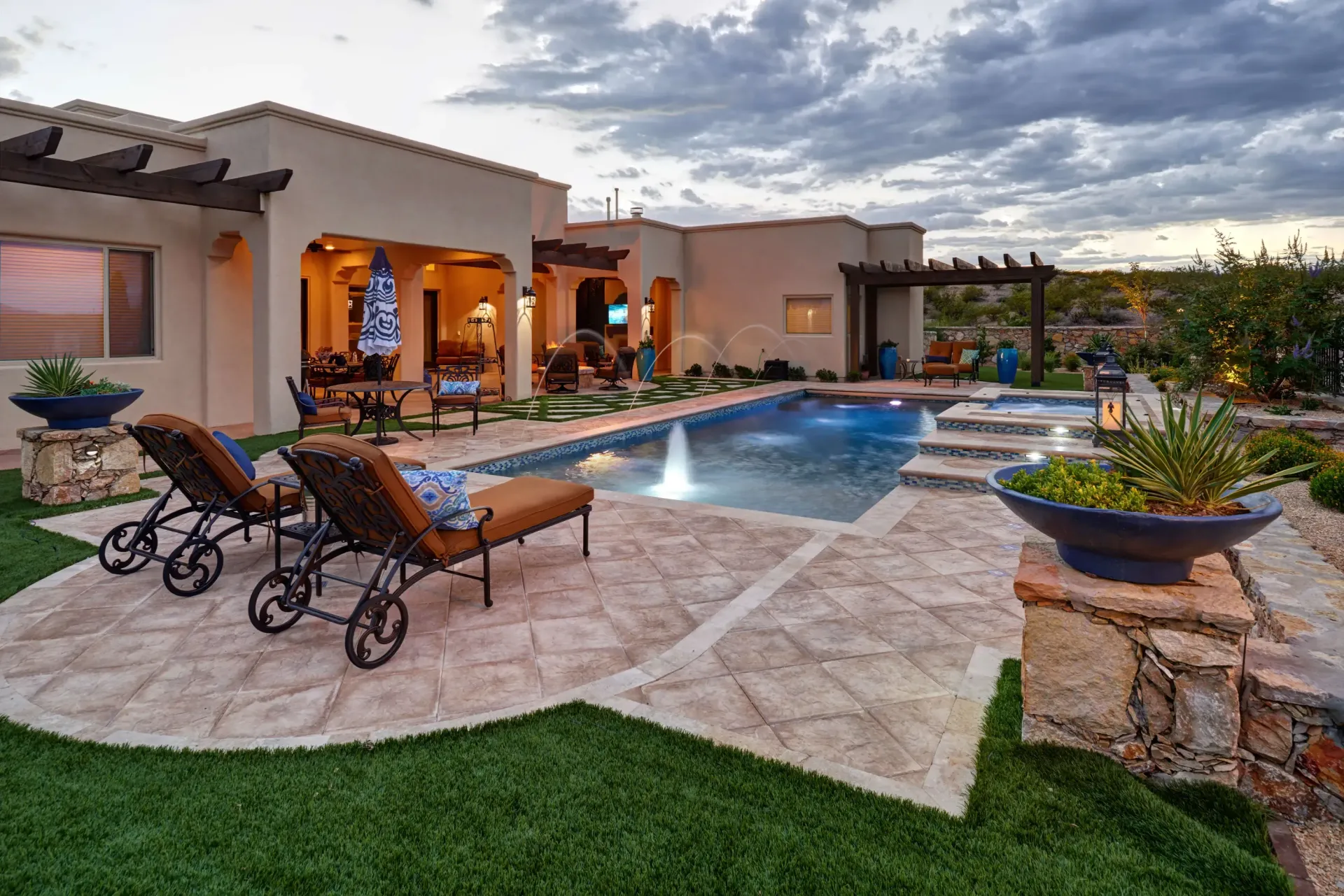 Backyard with pool, patio, and lounge chairs; warm-toned stucco house under a cloudy sky.