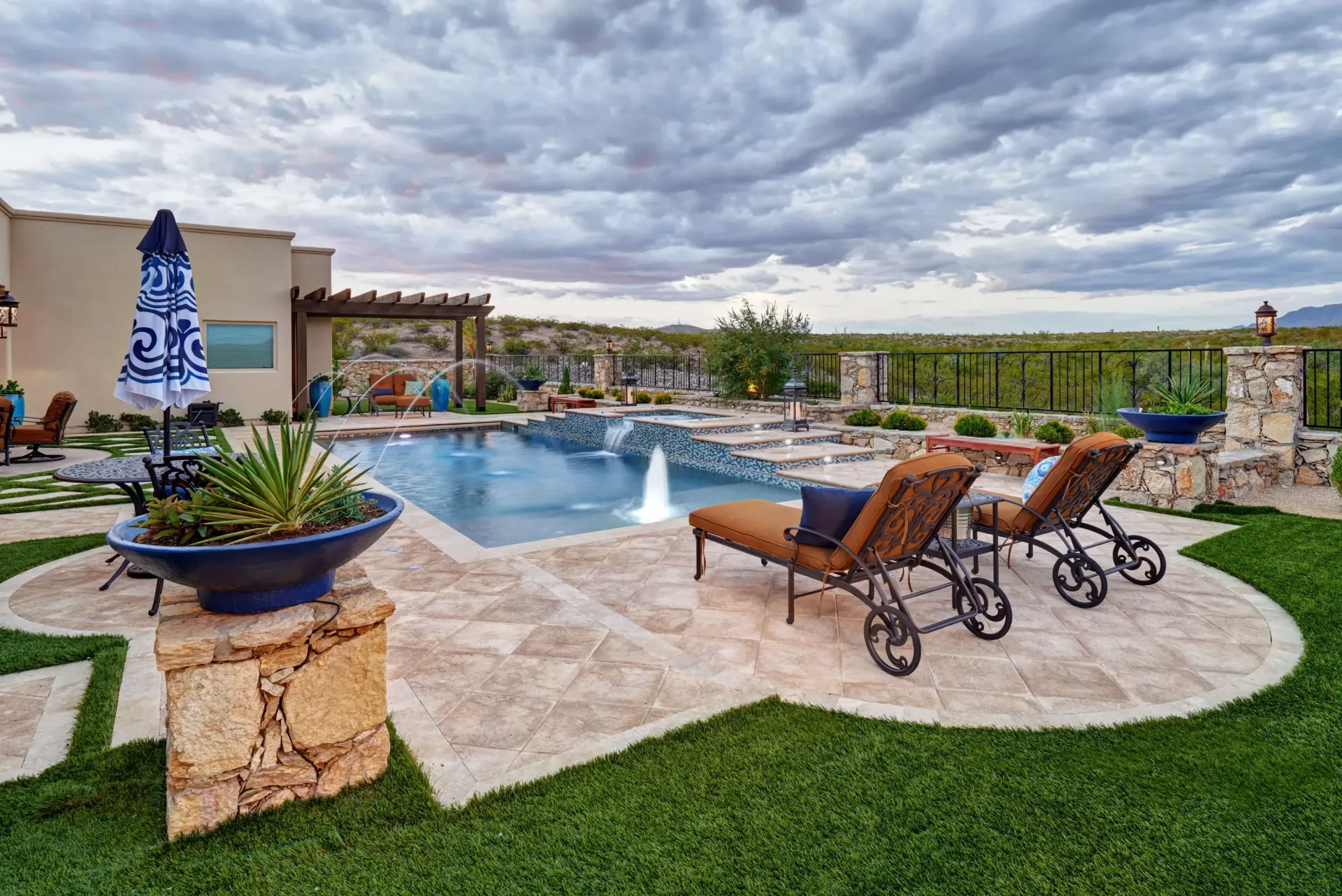 Luxury backyard with a swimming pool, lounge chairs, and lush landscaping under a cloudy sky.