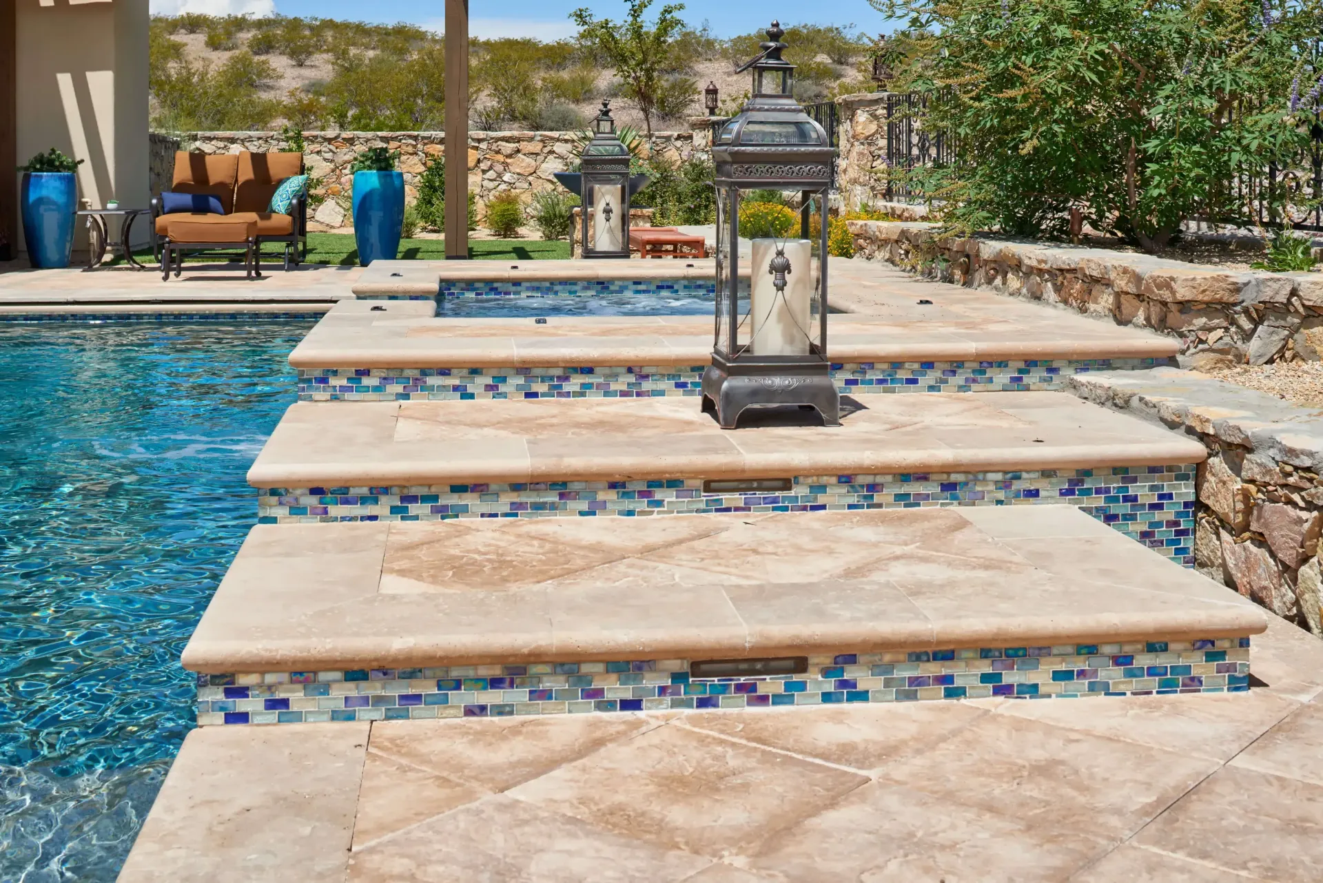 Pool steps with blue tile detail, stone patio, lantern, and surrounding desert landscape.