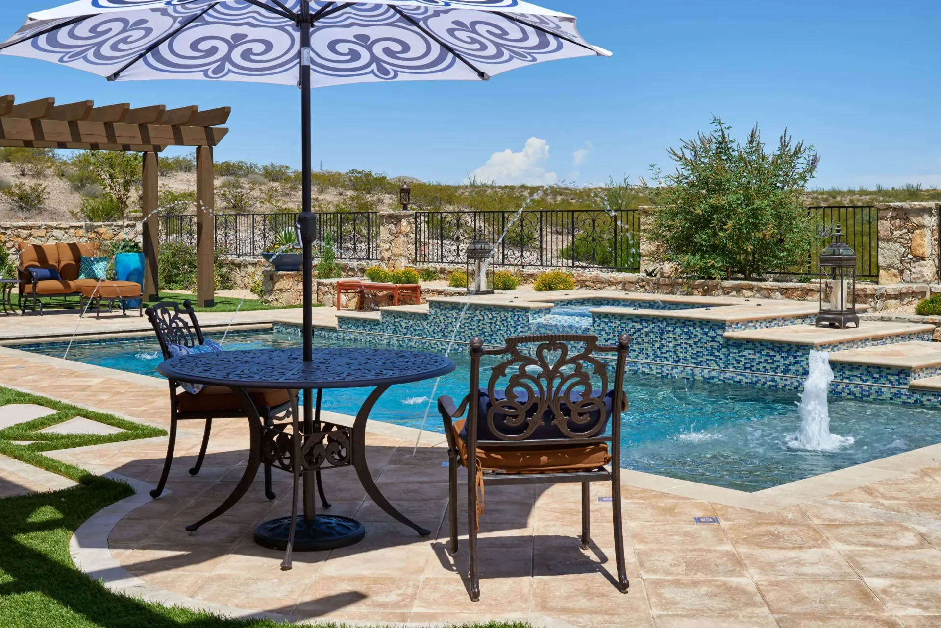 Patio with pool, table, and chairs under umbrella; sunny day.
