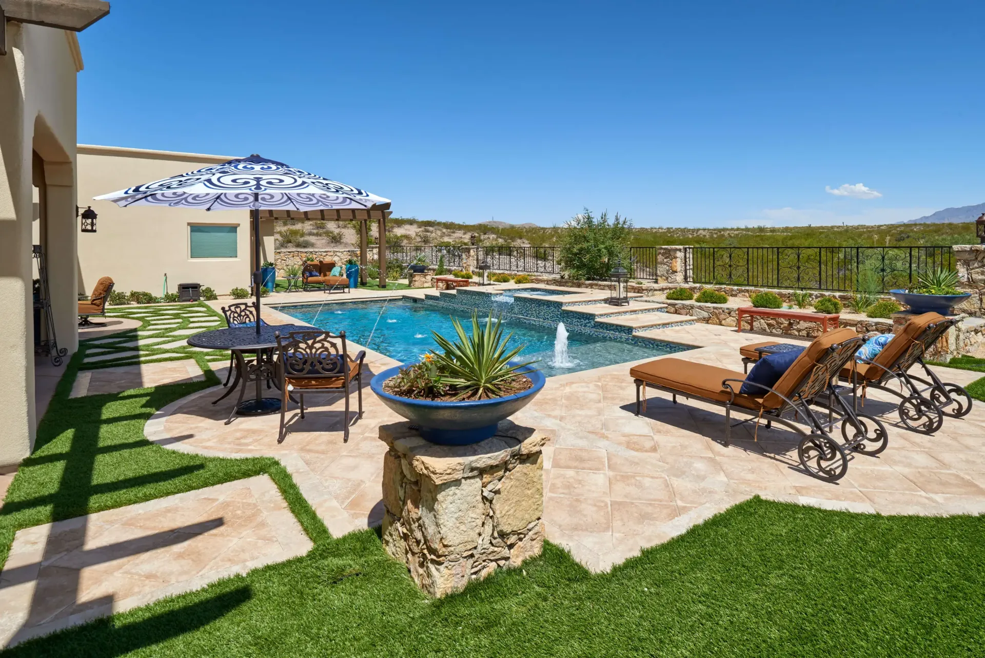 Backyard pool with lounge chairs, umbrella, and a blue sky.
