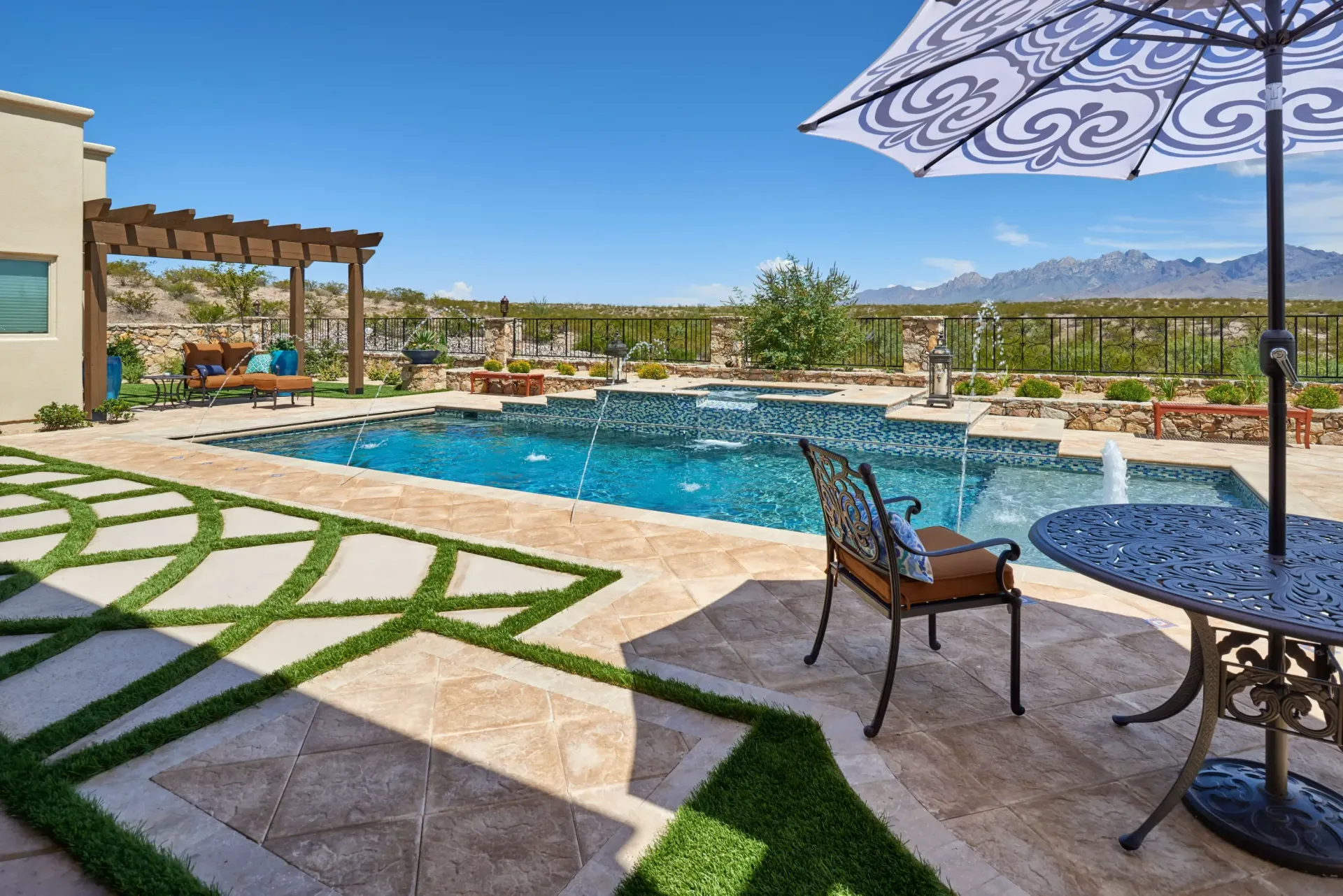 Backyard with pool, patio furniture, and artificial grass design; mountains in the background under a blue sky.