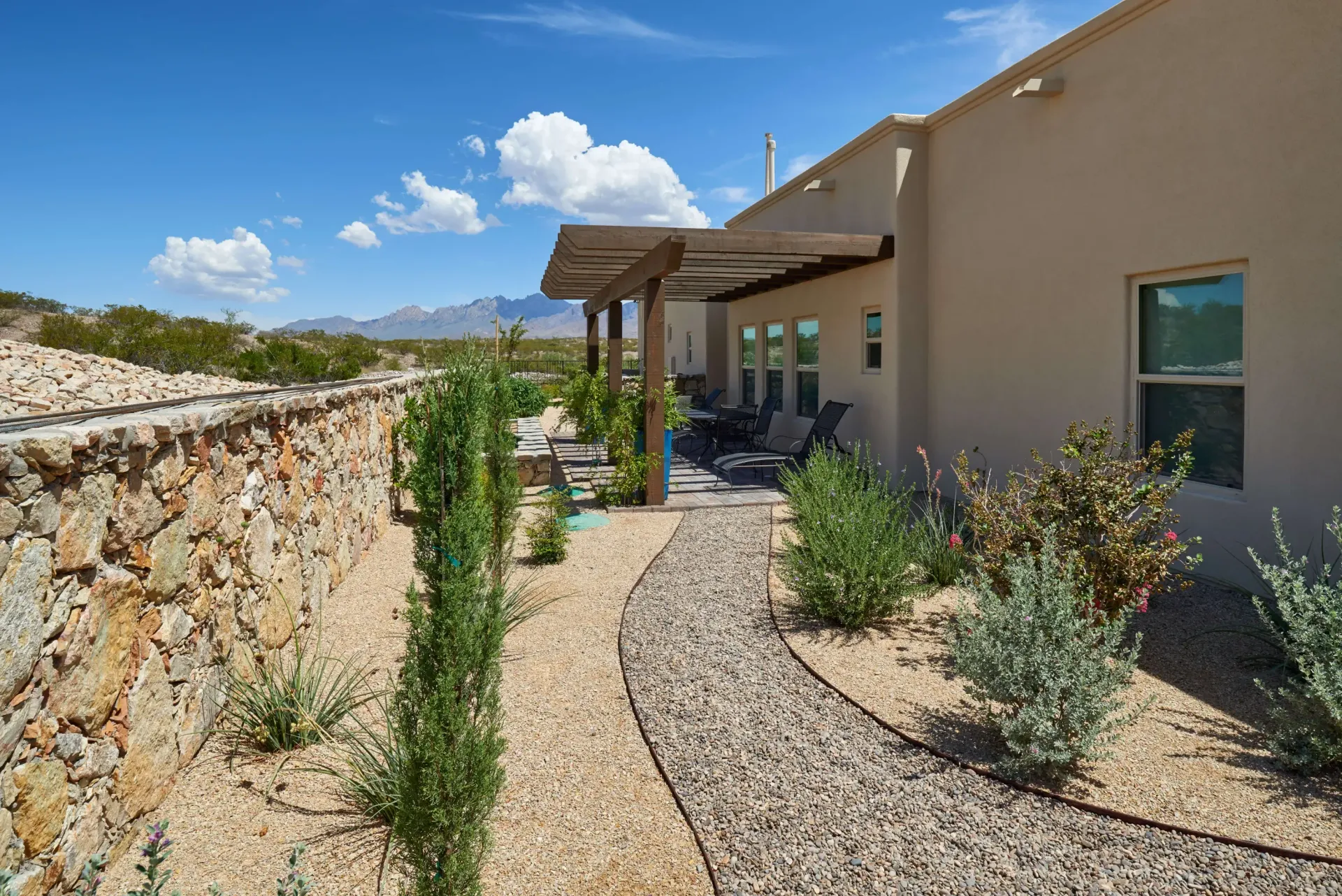 Stone pathway leads to a shaded patio beside a tan stucco house under a blue sky.