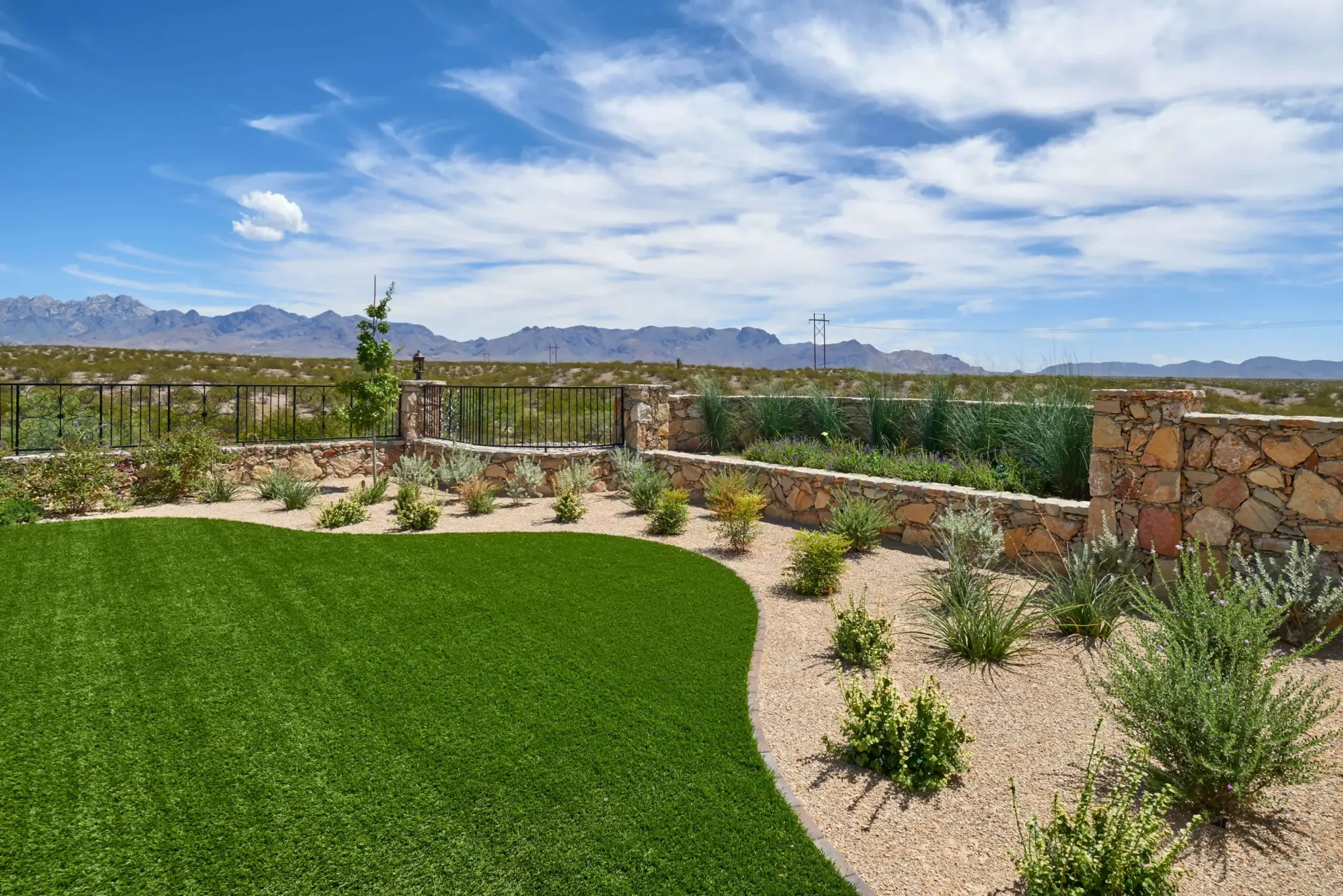 Green lawn with desert landscaping, stone wall, mountains, and blue sky.