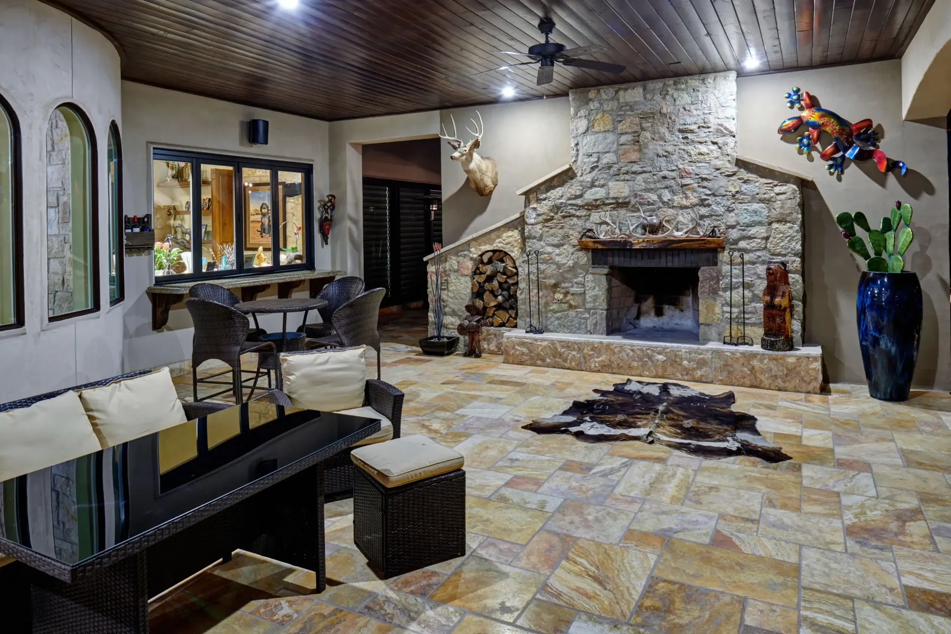 Patio with stone fireplace, wood ceiling, tile floor, outdoor furniture, and decorative items.