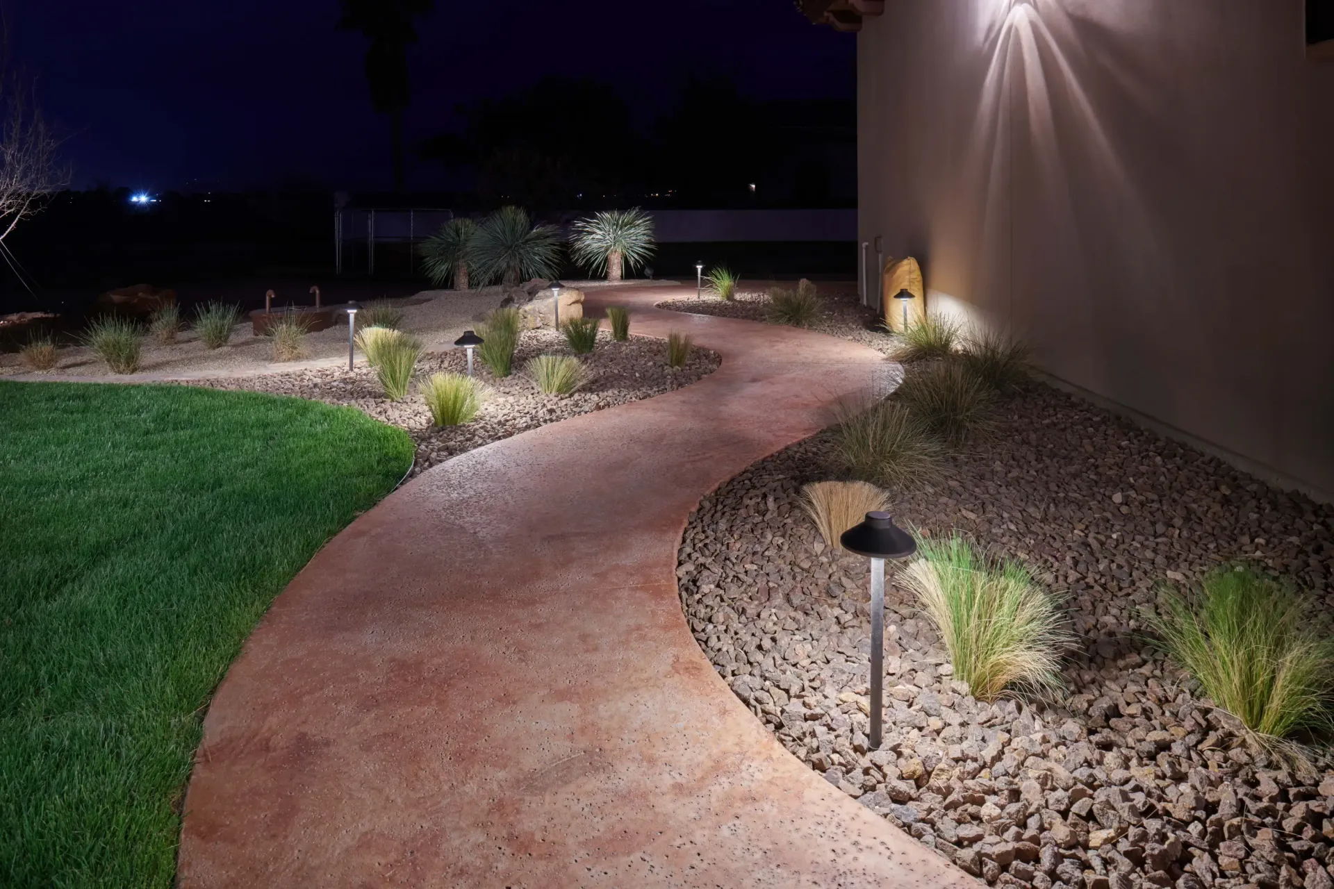 Pathway with landscape lighting at night, illuminating a curved walkway and surrounding greenery.