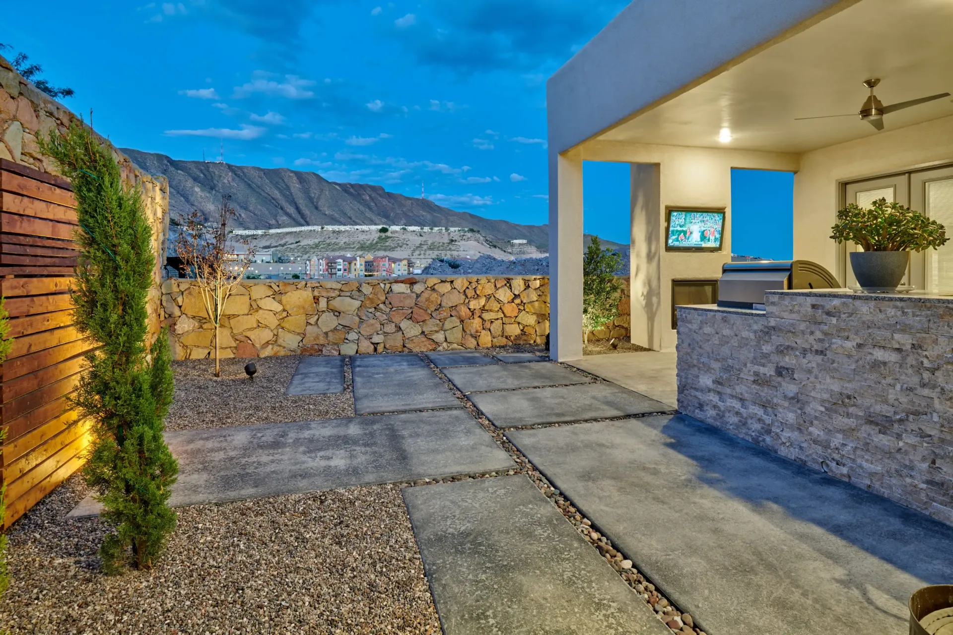 Patio with stone pavers, stacked wood wall, and view of mountains under twilight sky.