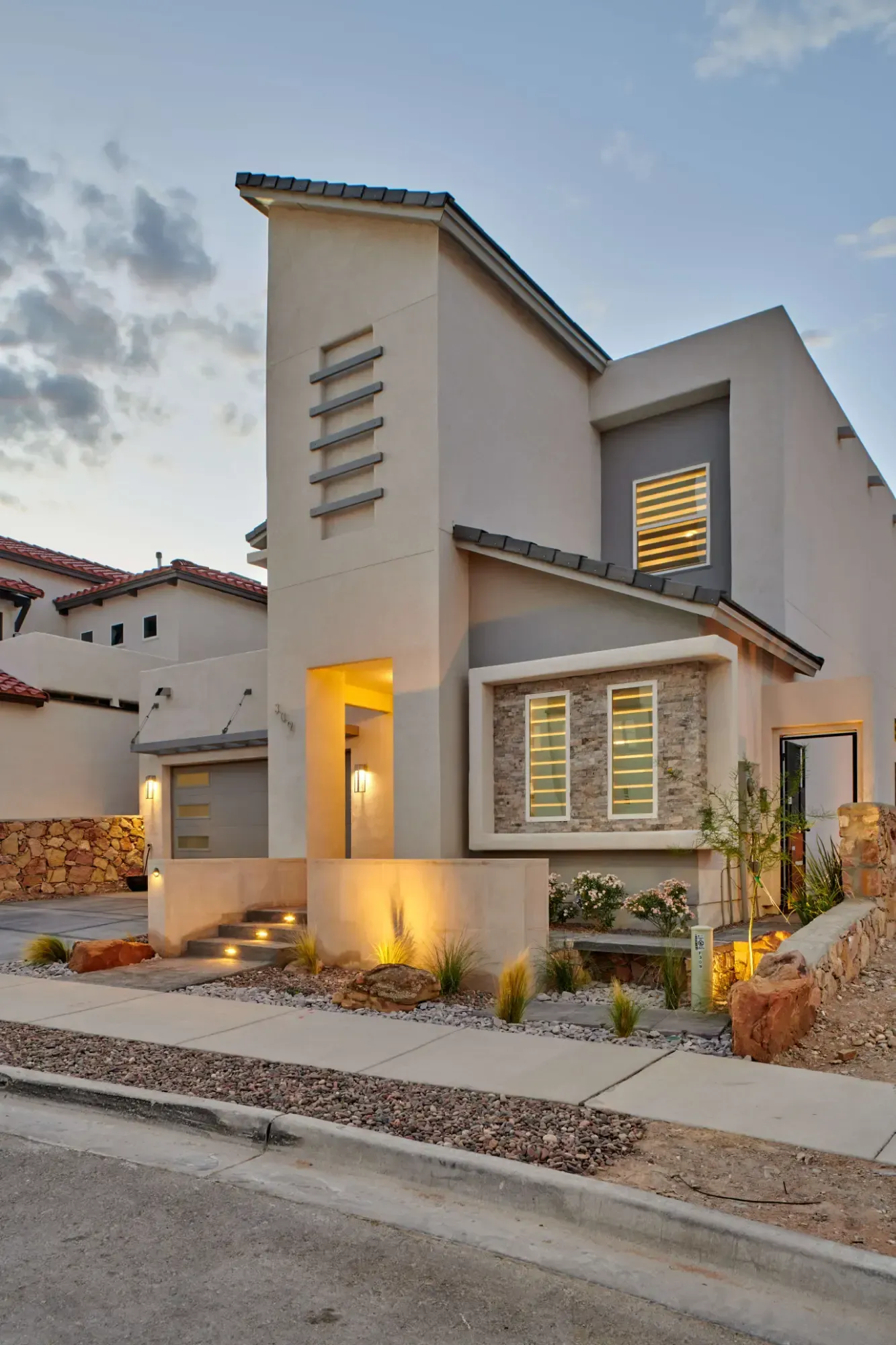 Modern two-story stucco home with a beige exterior, a gray roof, and landscaping.
