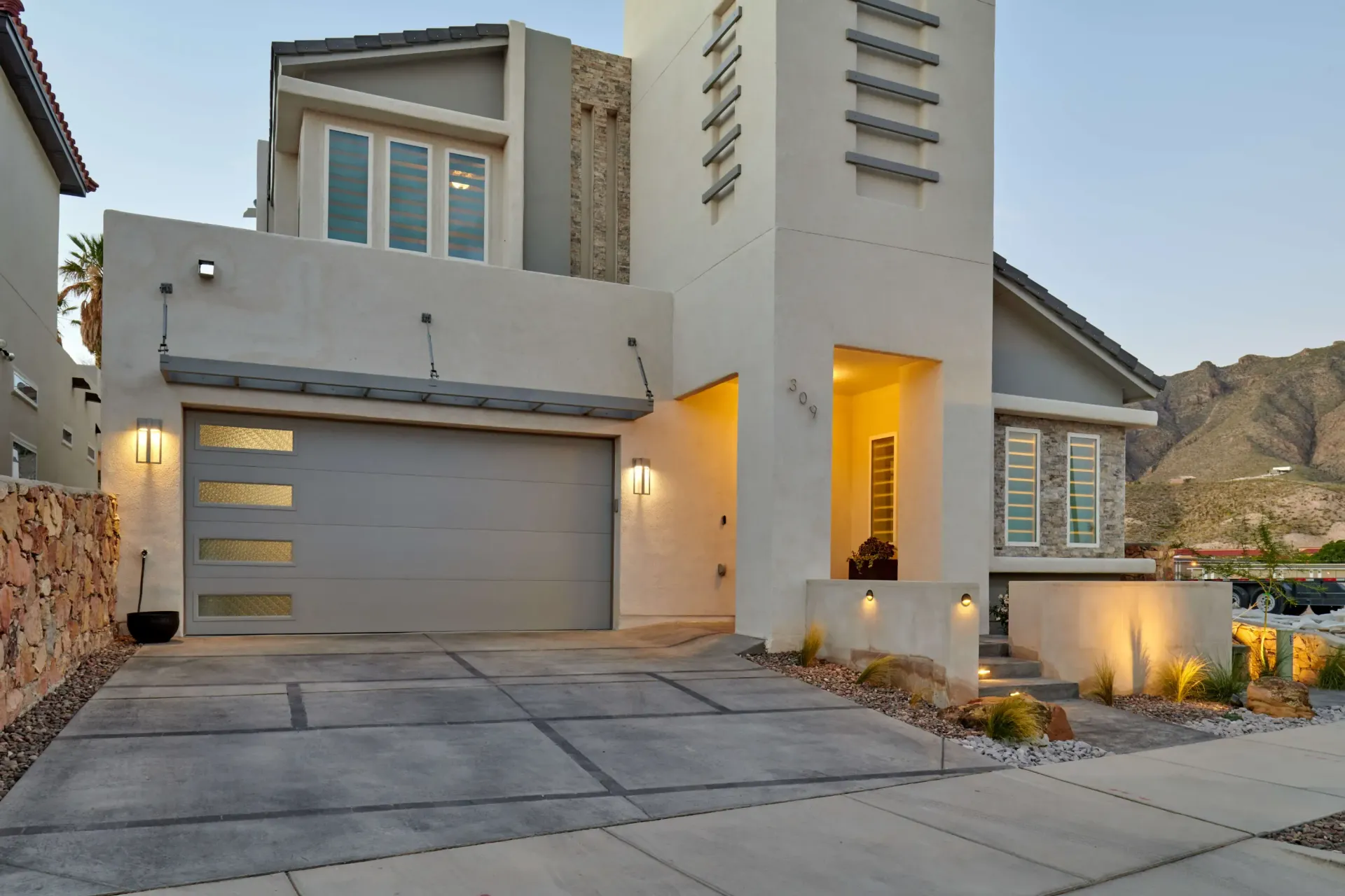 Modern two-story house with gray garage door, stucco exterior, and mountain backdrop.