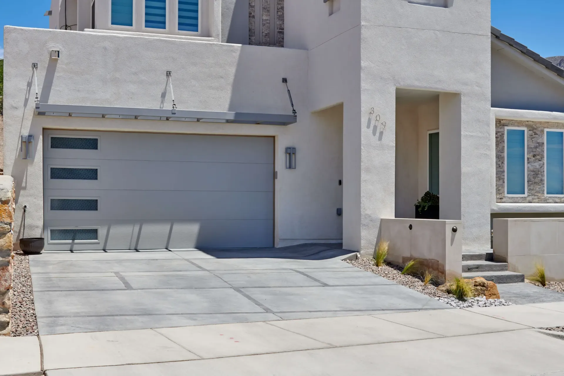 Modern two-story house with a grey garage door, concrete driveway, and a white stucco exterior.