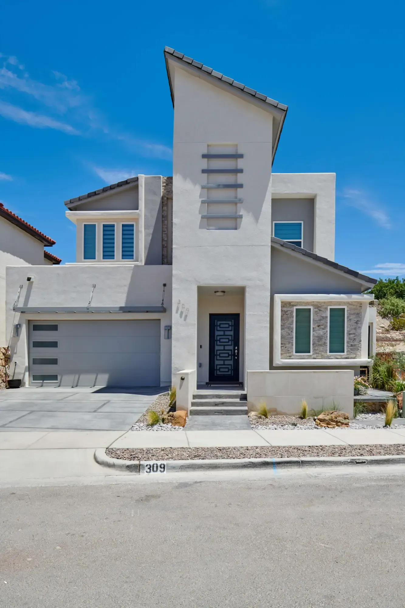 Modern two-story house with gray stucco exterior, blue sky, and a curved driveway.
