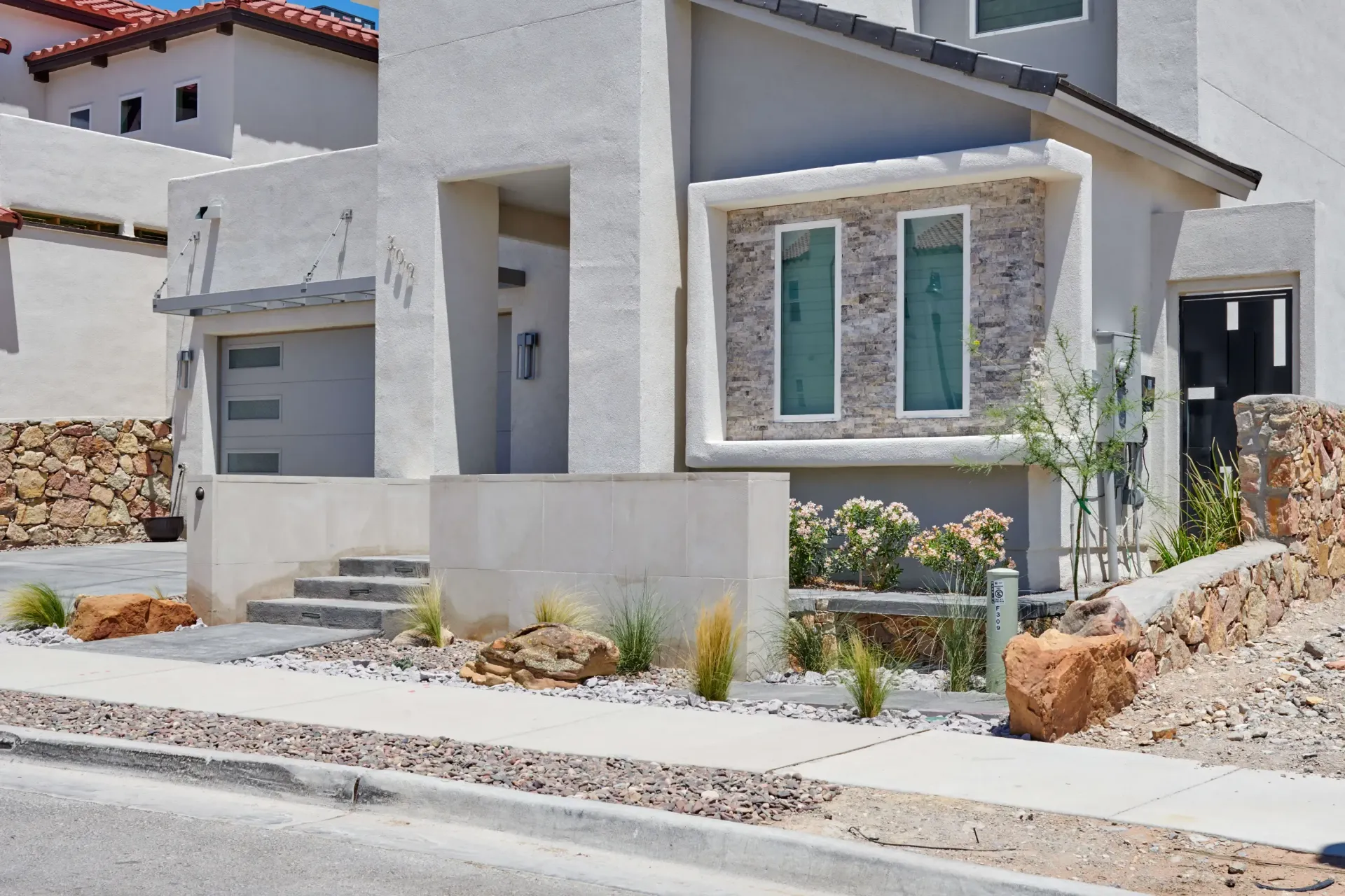 Modern light gray house with stone accents, small front yard, and sidewalk.