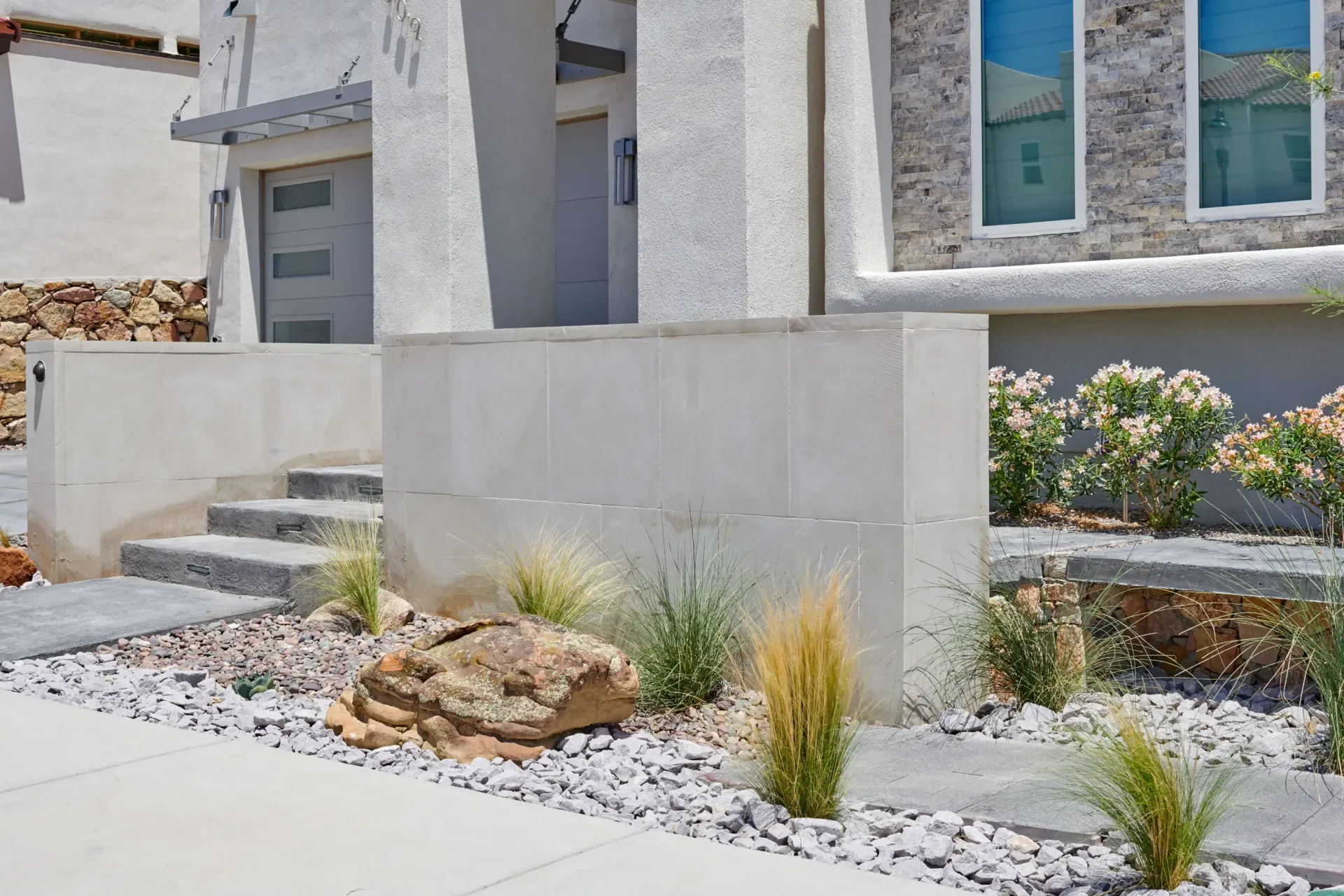 Exterior of a modern home with concrete pillars, steps, and landscaping featuring rocks and greenery.