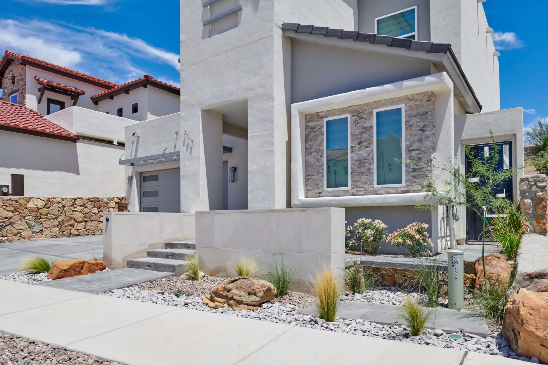 Modern two-story house with light stucco exterior, stone accents, and drought-tolerant landscaping.