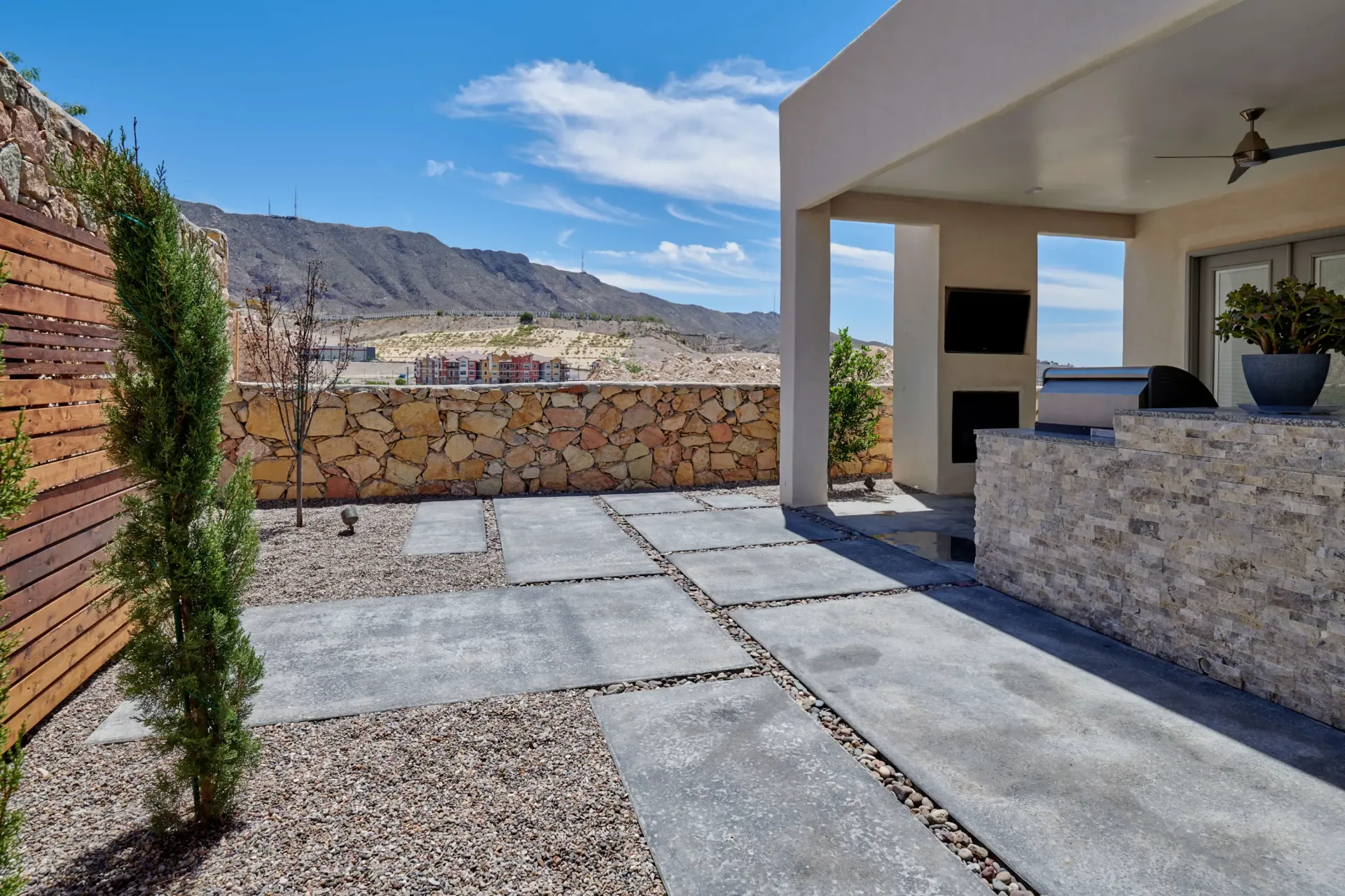 Patio with stone wall, concrete pavers, gravel, and mountain view. Sunny day.