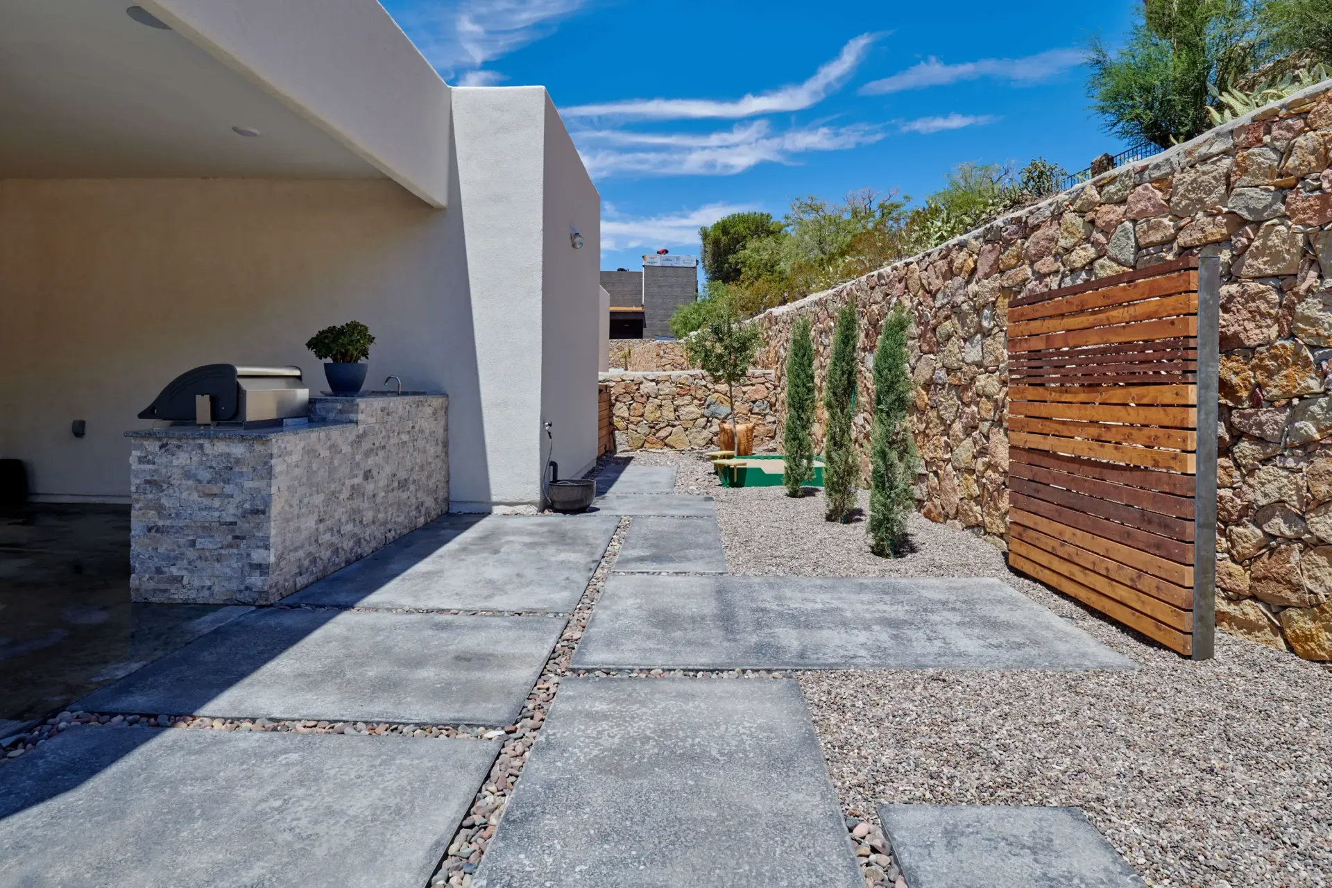 Outdoor patio with stone wall and concrete path leading to wooden gate.