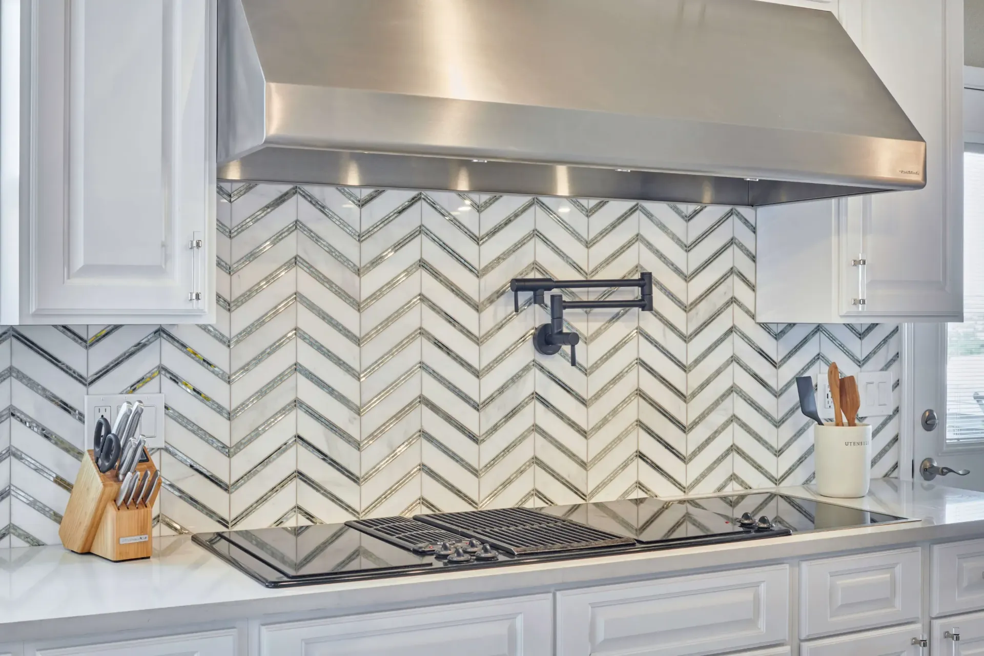 Kitchen with white cabinets, stainless steel range hood, and herringbone tile backsplash.