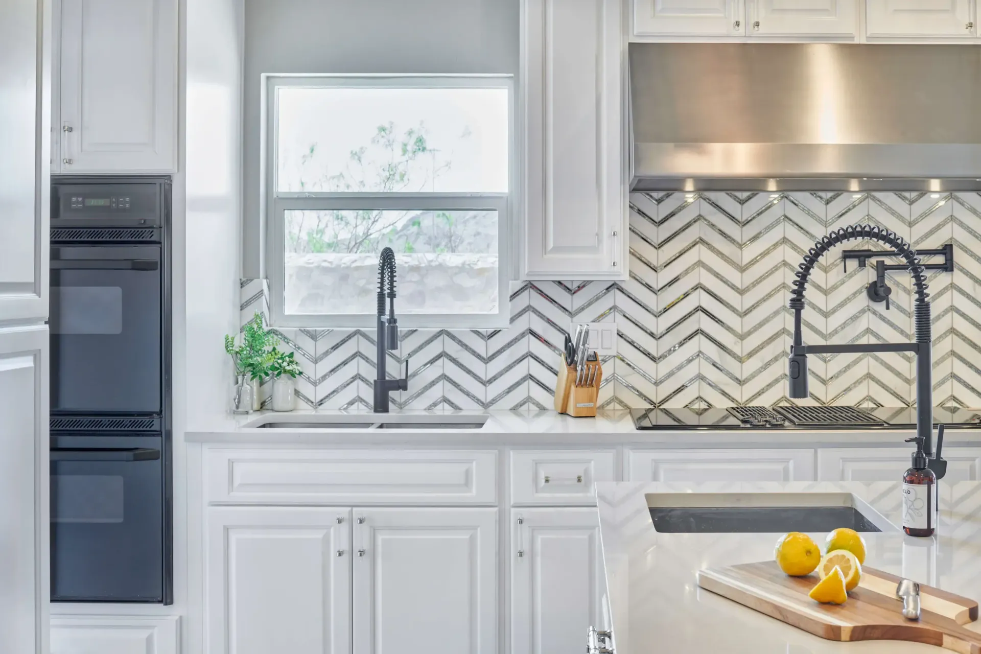 White kitchen with chevron tile backsplash, stainless steel appliances, and black faucet.