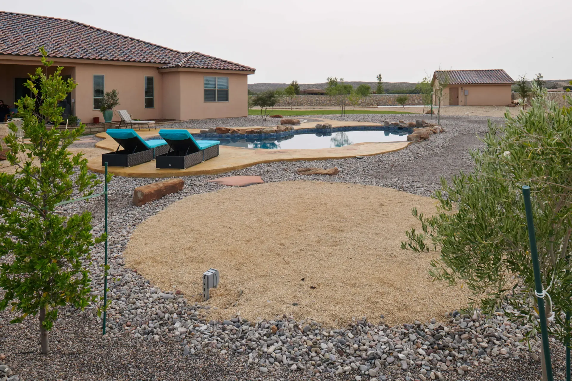 Backyard with a pool, lounge chairs, and landscaping; a house is in the background.