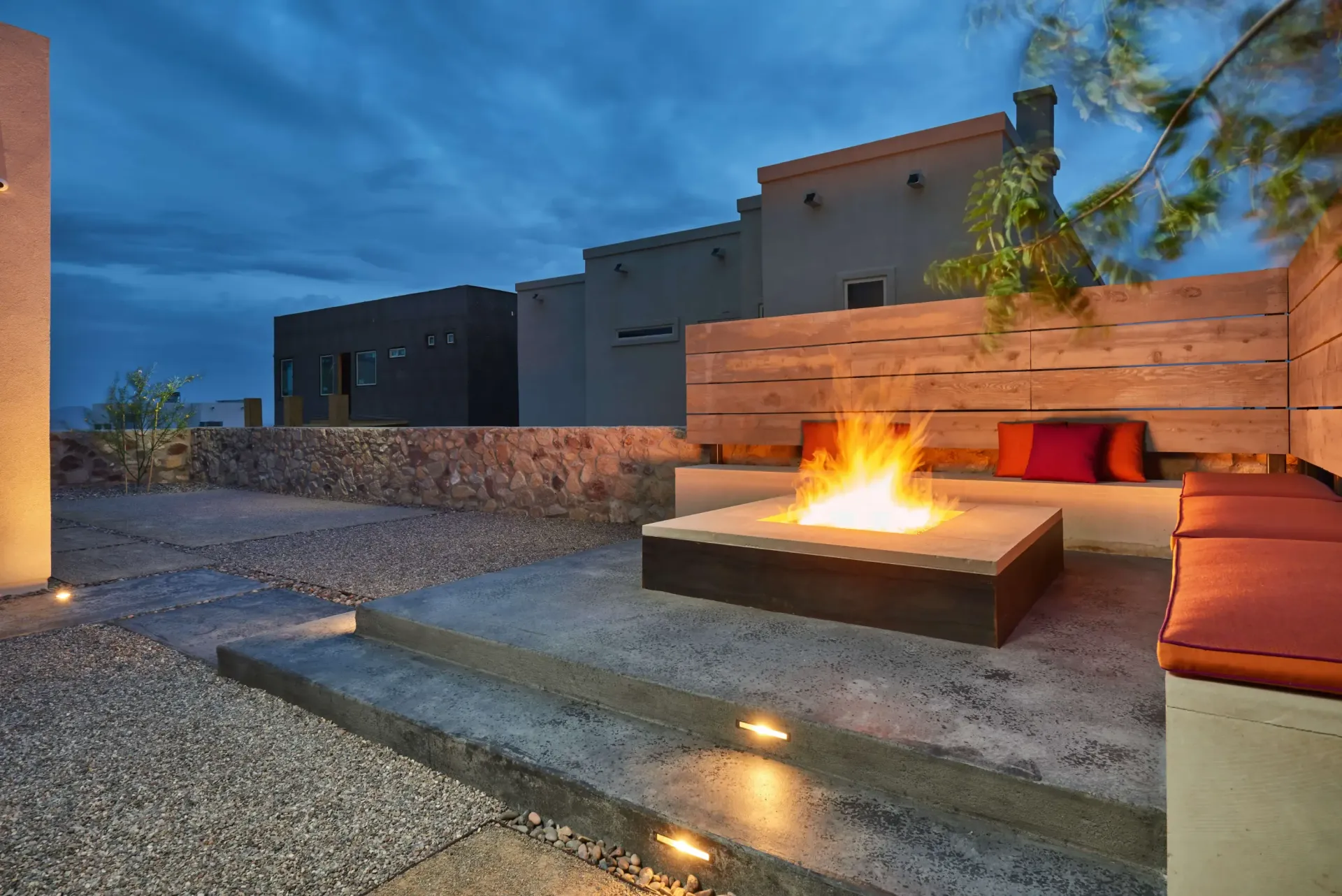 Outdoor fire pit with seating, house in background, twilight sky.