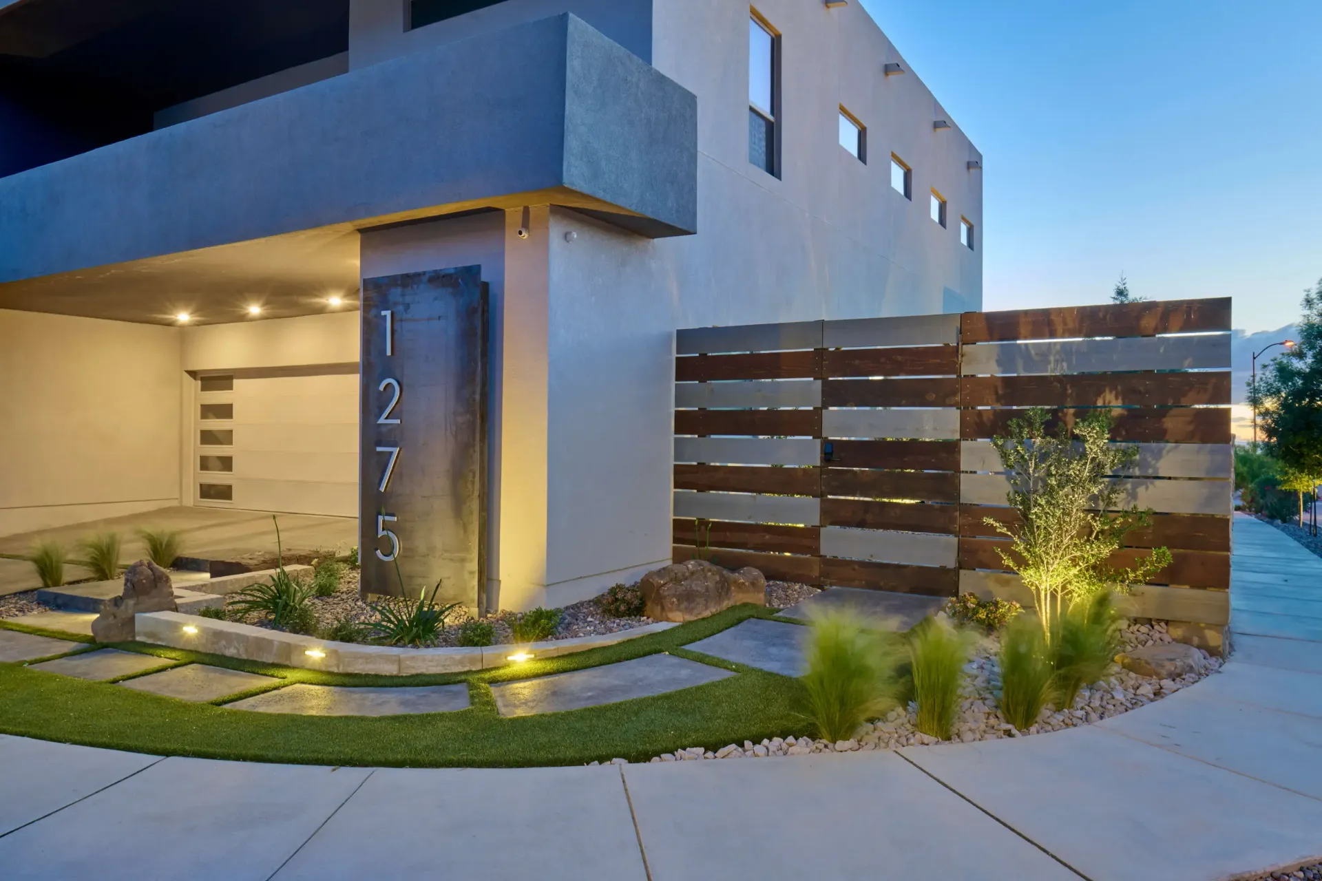 Modern home exterior with address marker, stone pathway, wooden fence, and landscape lighting.