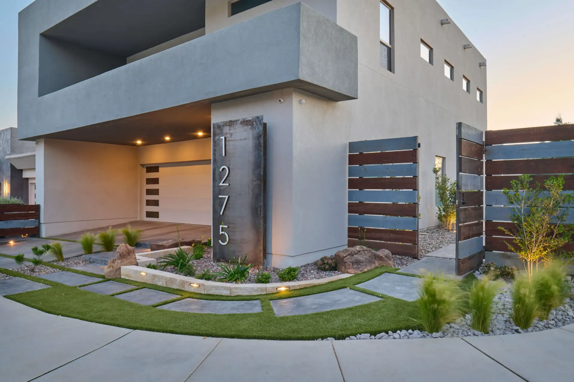 Modern home exterior with gray stucco, wooden accents, and a landscaped yard. Address marker