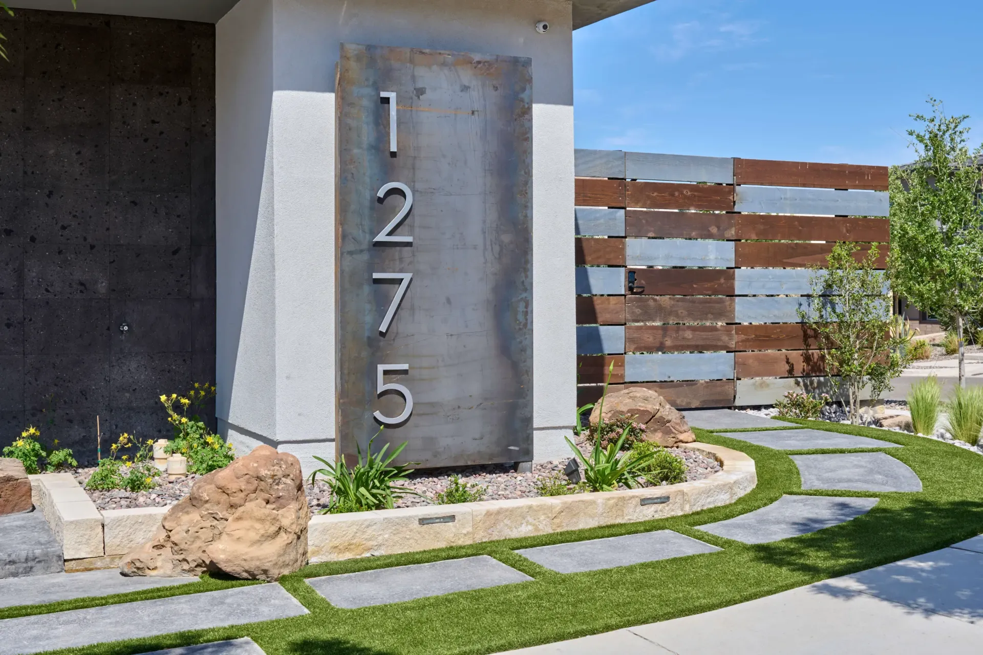 Metal address sign on a modern home facade with landscaping, featuring the number
