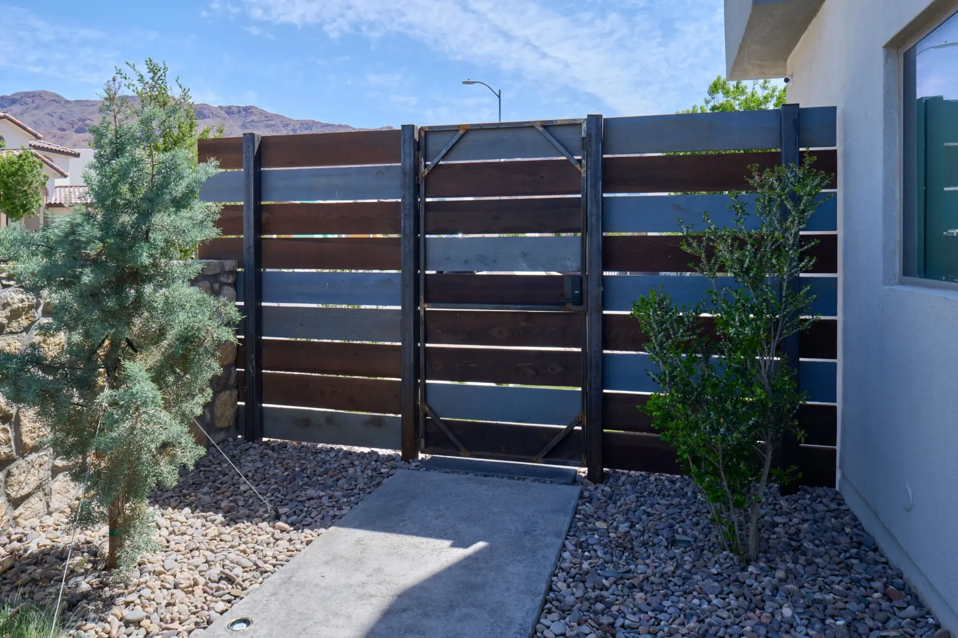 Wooden fence with gate; front yard with plants and a concrete walkway. Brown, blue, and gray panels.