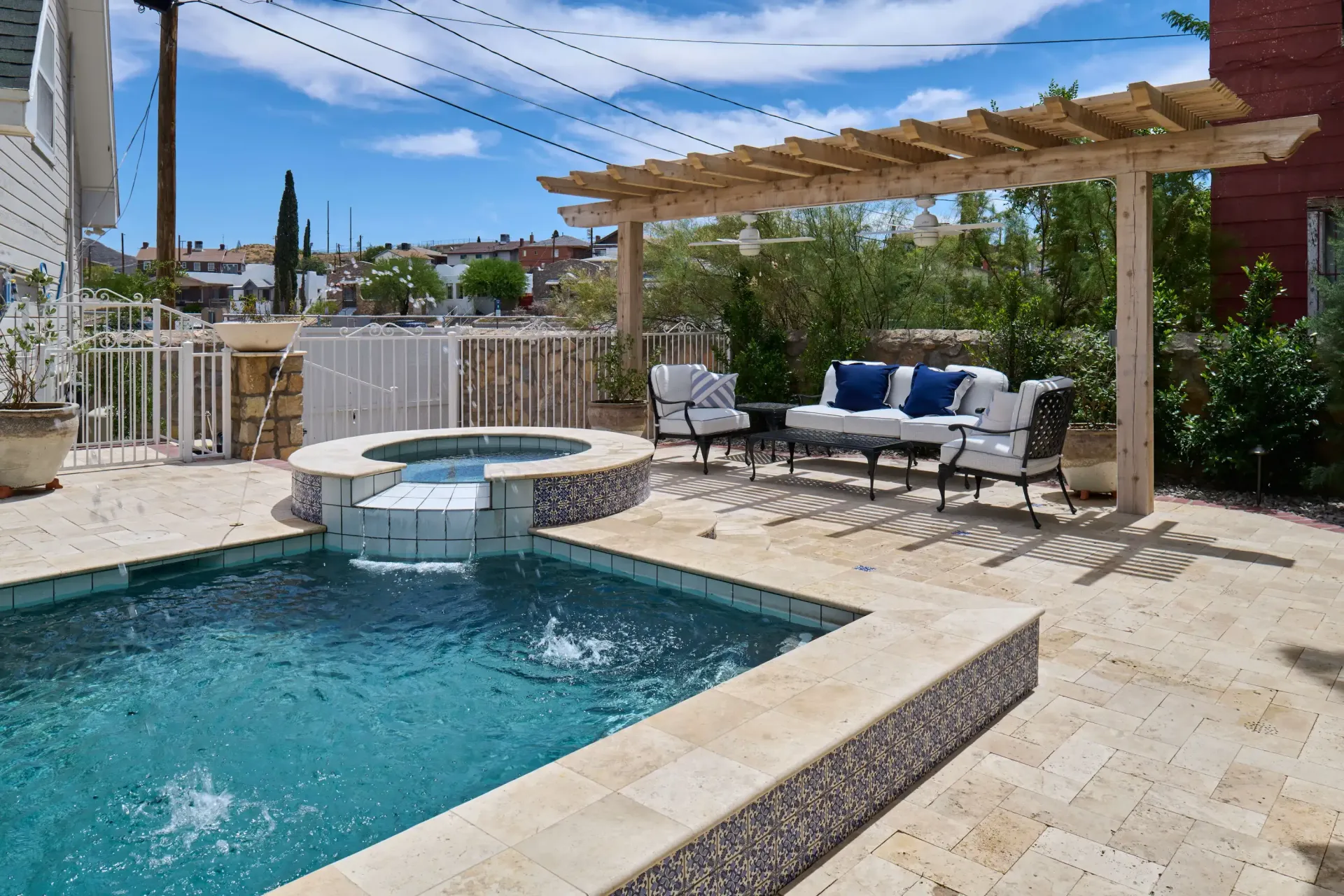 Backyard with pool, jacuzzi, and seating under a wooden pergola on a sunny day.