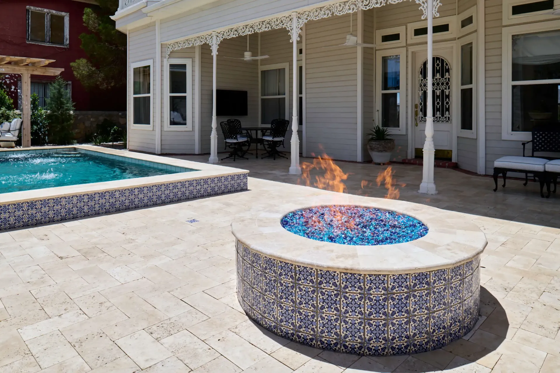 Outdoor patio with pool, fire pit, and white Victorian house in the background. Fire burning in the pit.