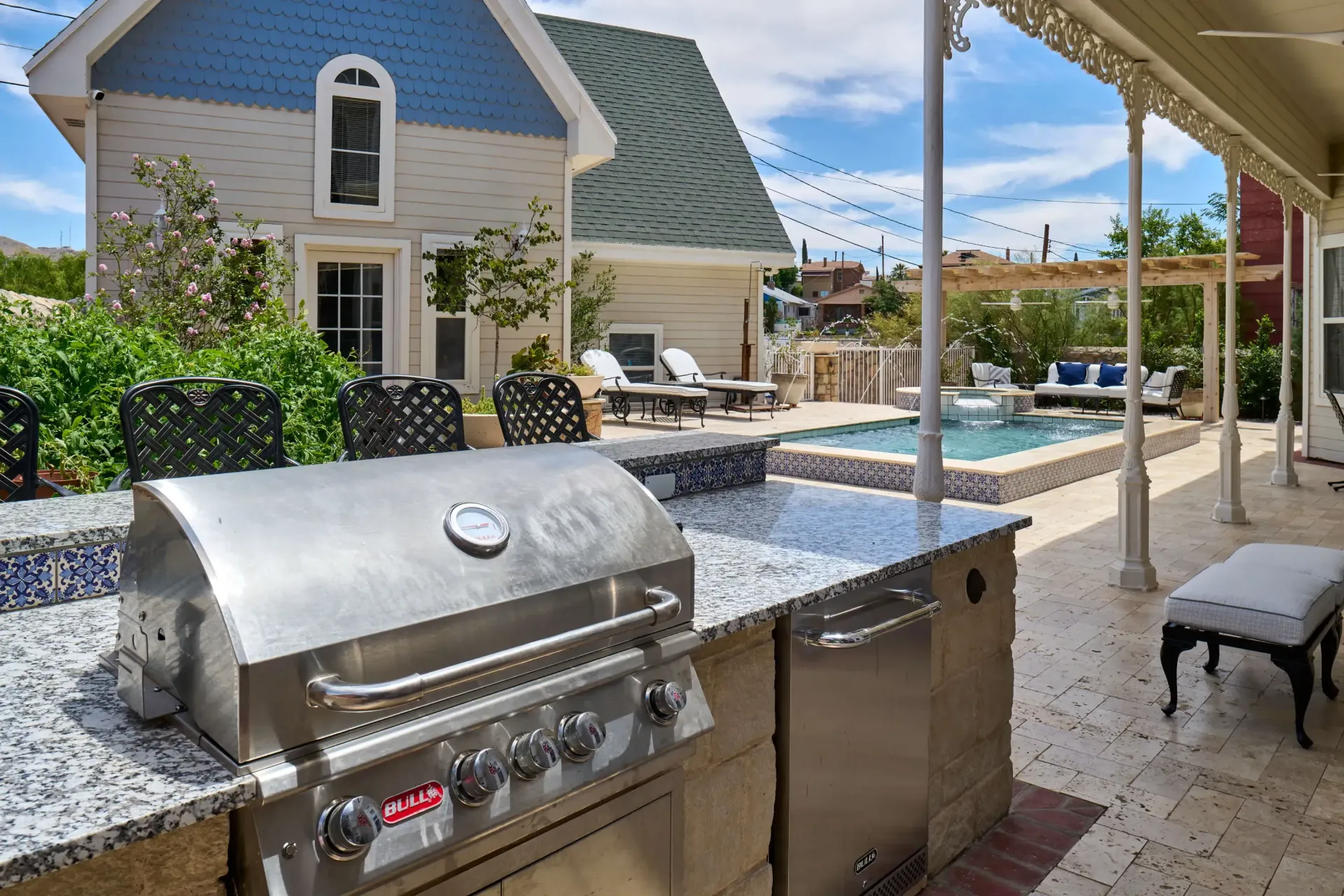 Outdoor kitchen with a stainless steel grill, a pool, and a two-story house with blue and gray siding.