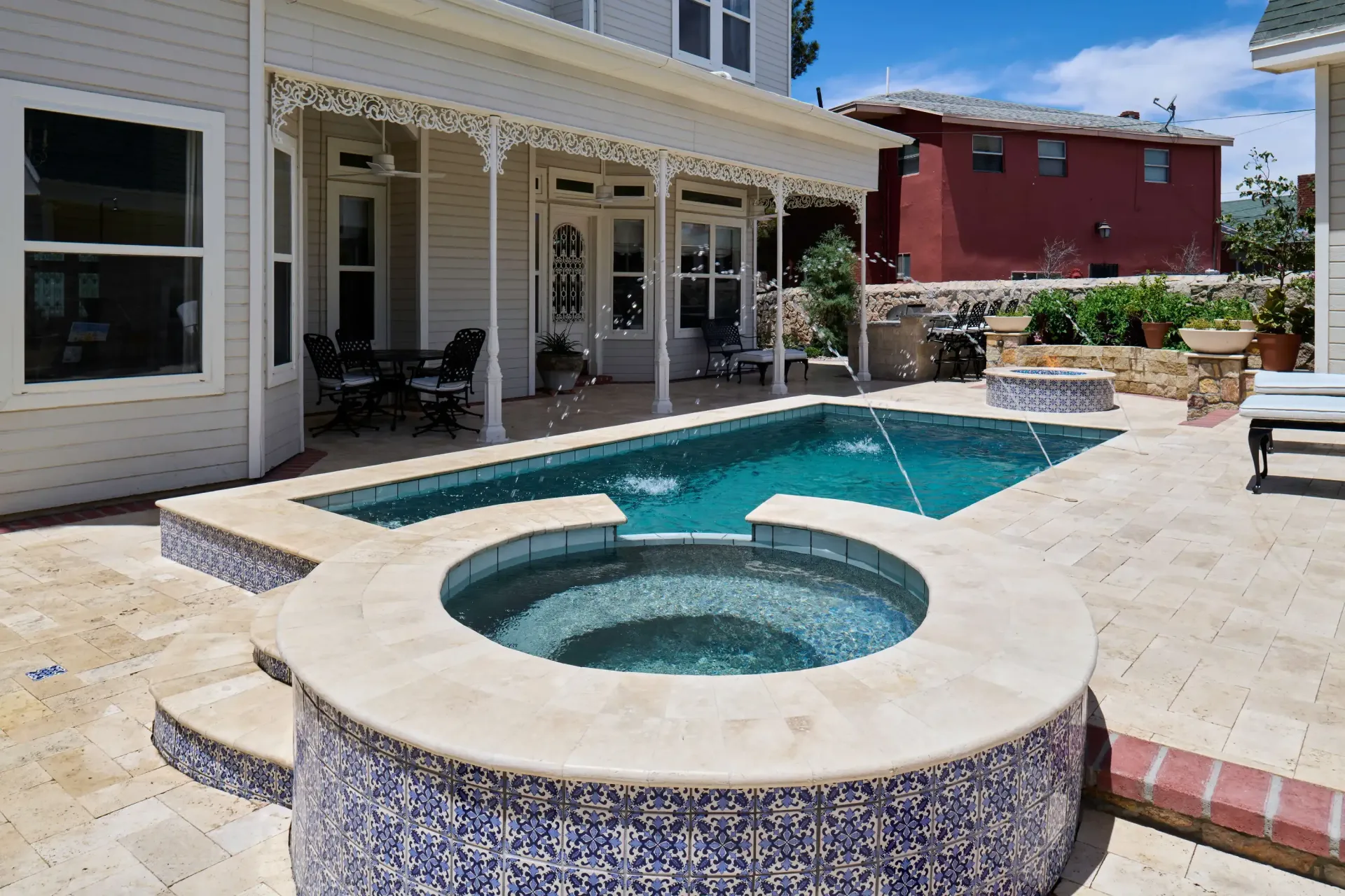 Pool and hot tub with stone surround in backyard of a white house.