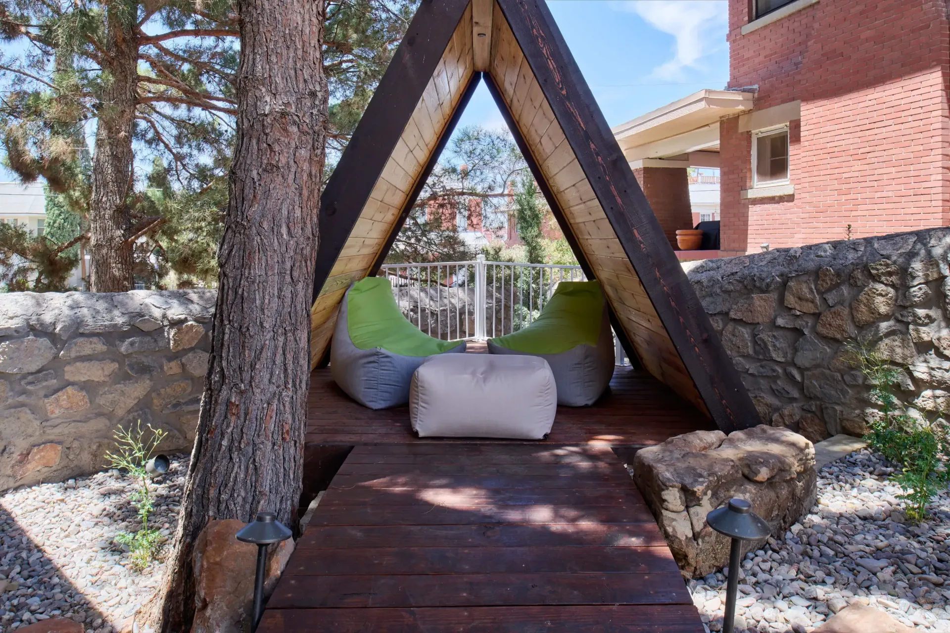 Triangular wooden shelter with two green beanbag chairs and beige ottoman on a wooden deck.