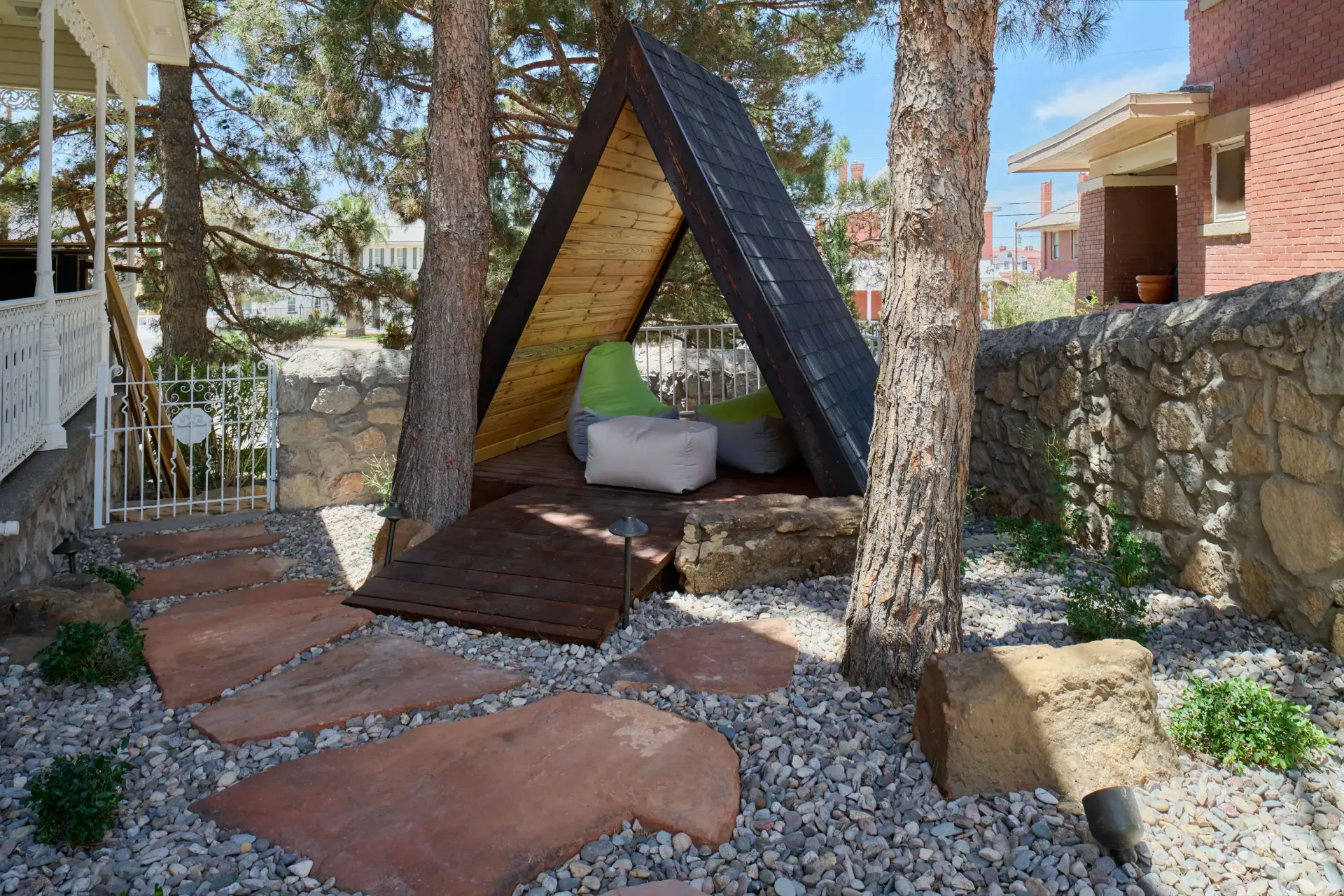 A-frame wooden structure with seating in a garden setting, accessed by stone path.