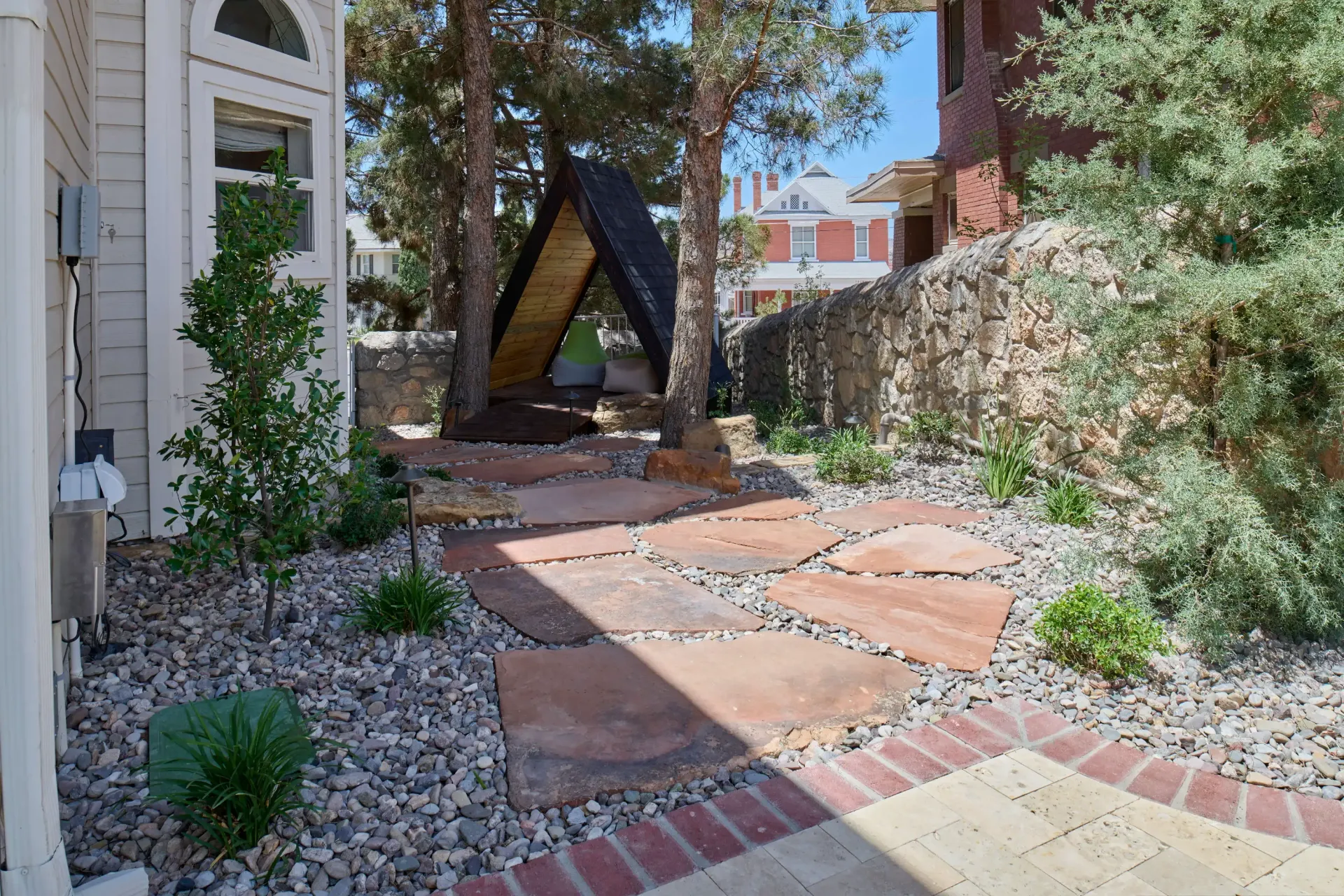 Stone path through a landscaped yard with a black A-frame structure and a brick building in the background.