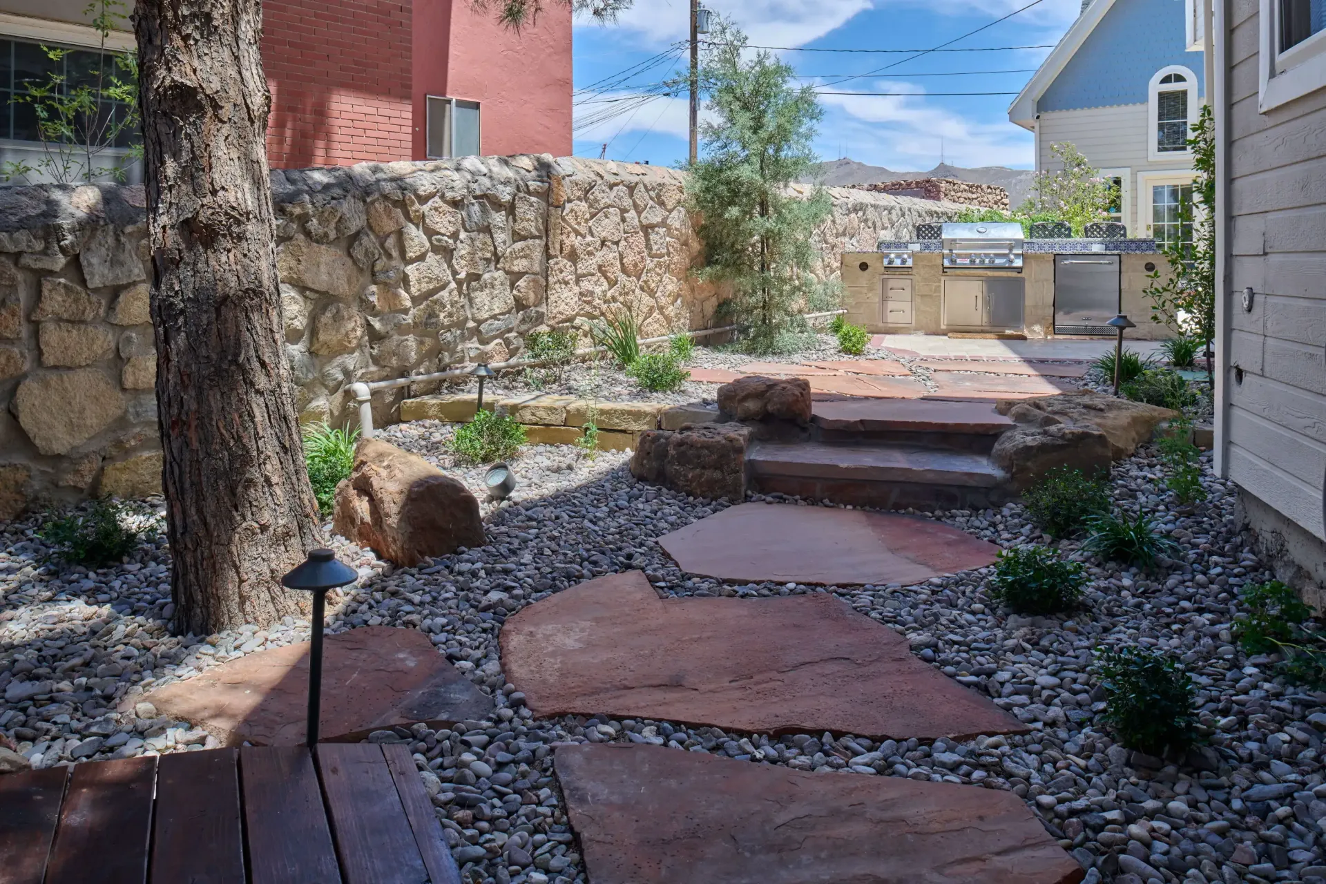 Flagstone pathway leading to an outdoor kitchen, surrounded by rocks and a stone wall.