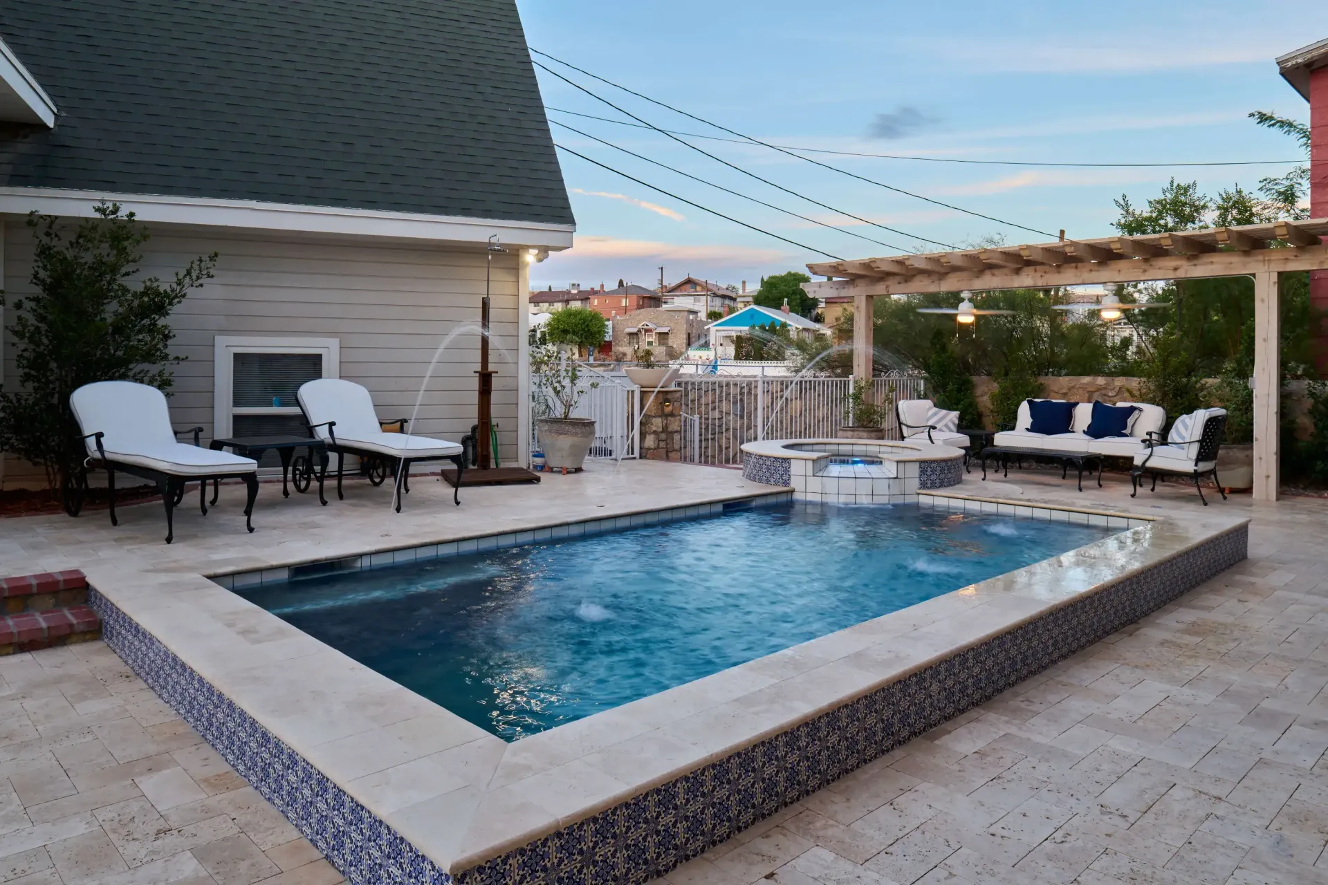 Rooftop patio with rectangular pool, seating, and pergola. Blue and white accents, cloudy sky.