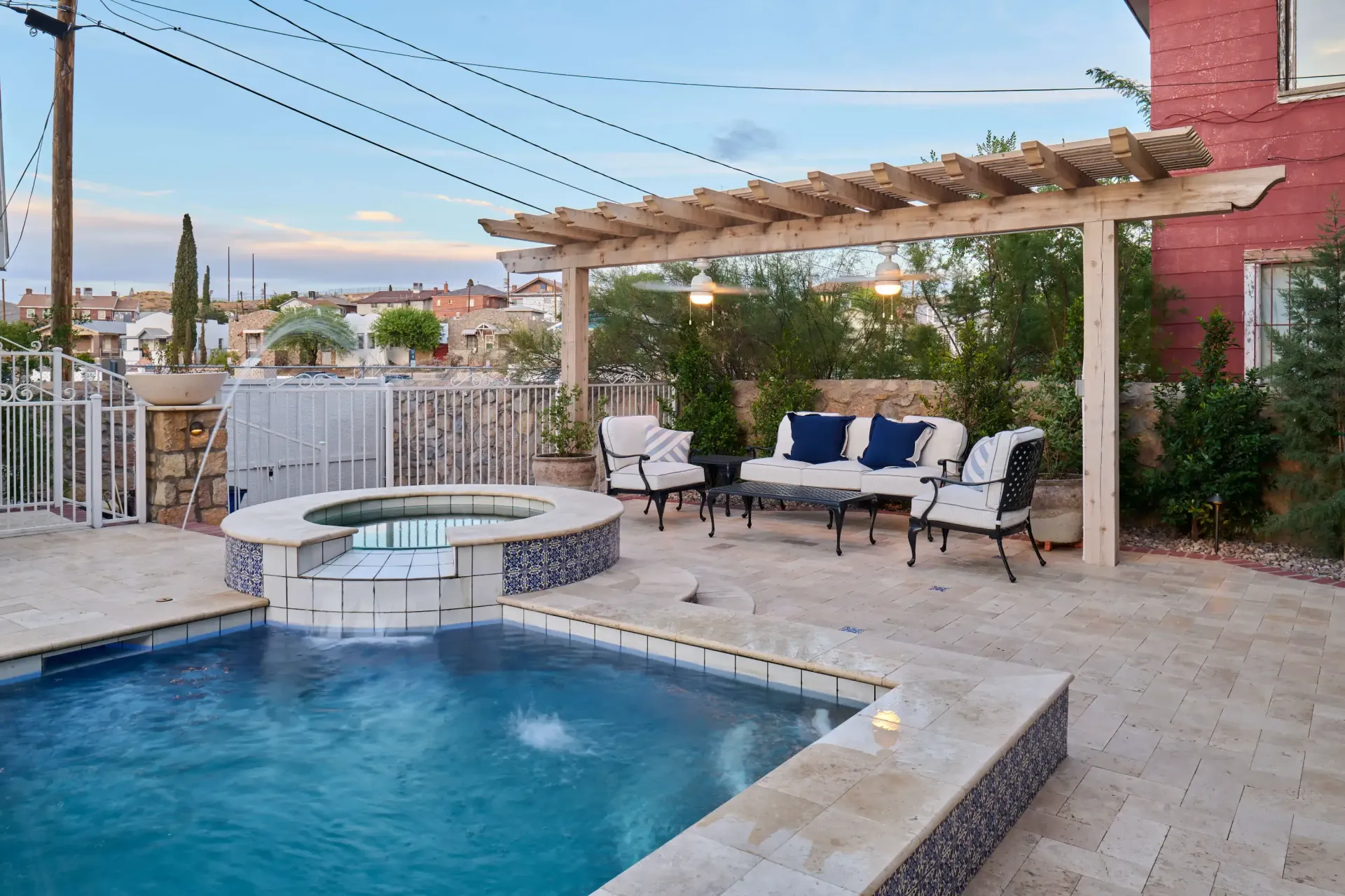 Backyard with a pool, hot tub, and seating area under a wooden pergola with string lights.