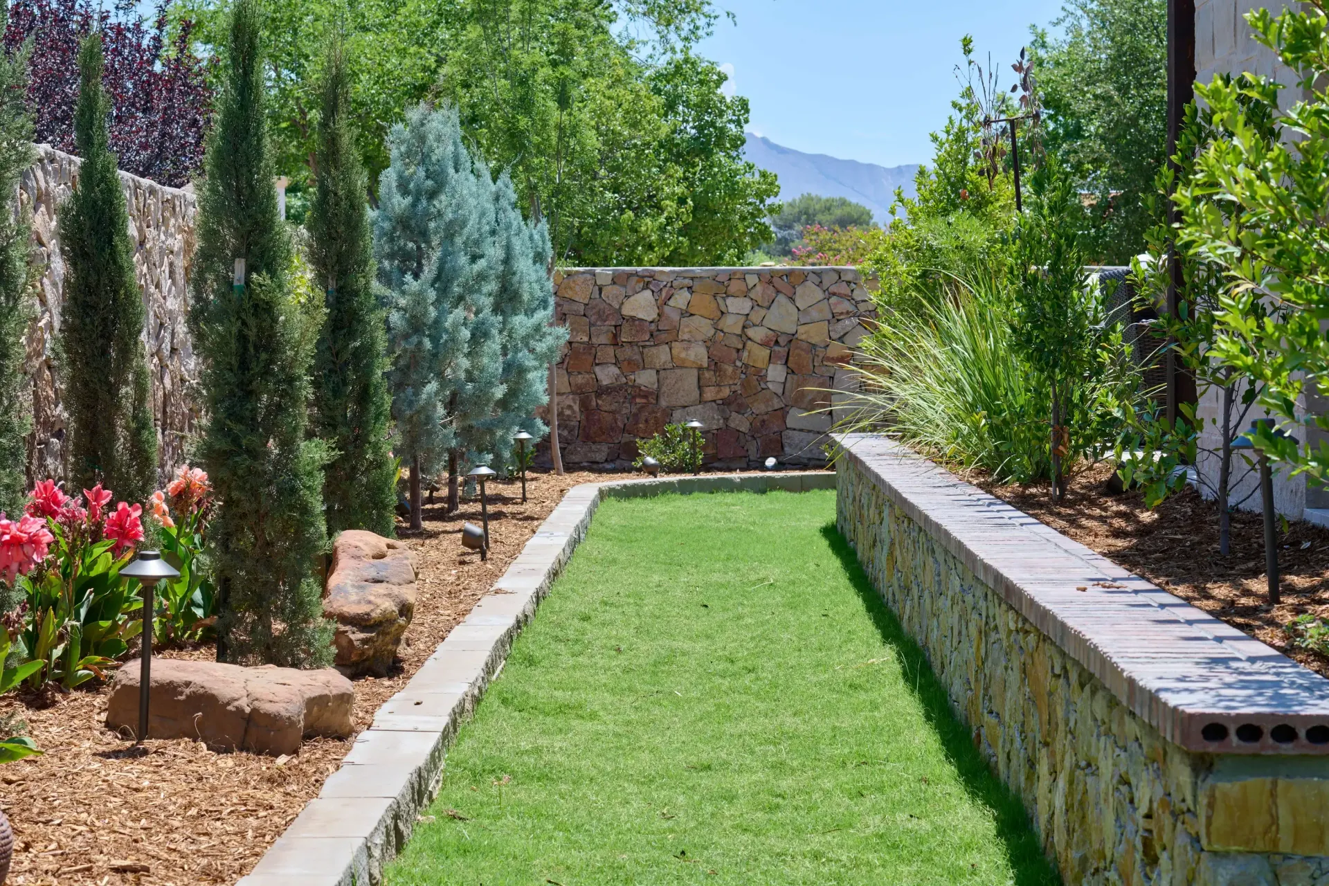 Pathway of grass and gravel with trees and stone walls in a garden.