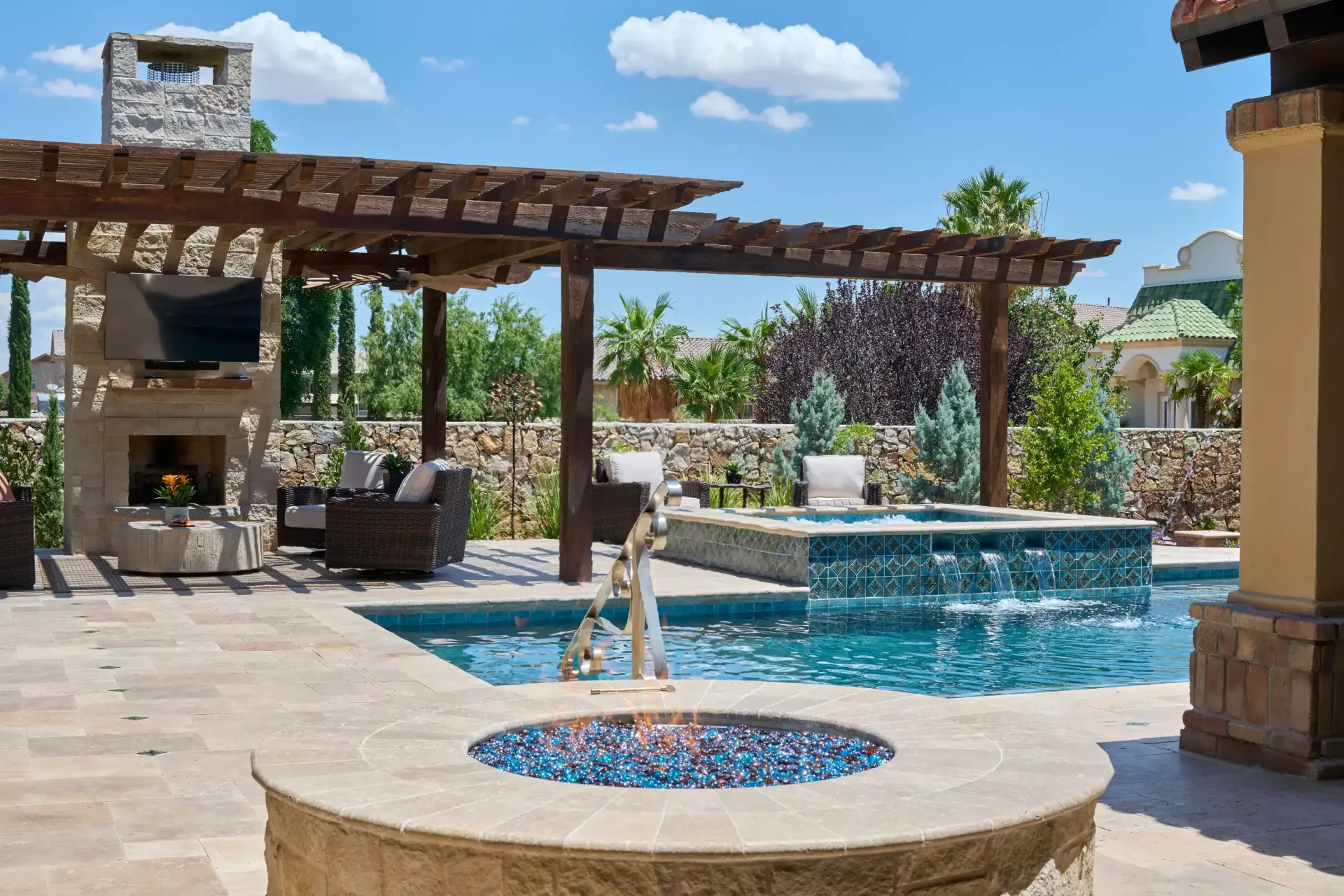 Luxurious backyard with pool, spa, fireplace, and pergola on a sunny day.