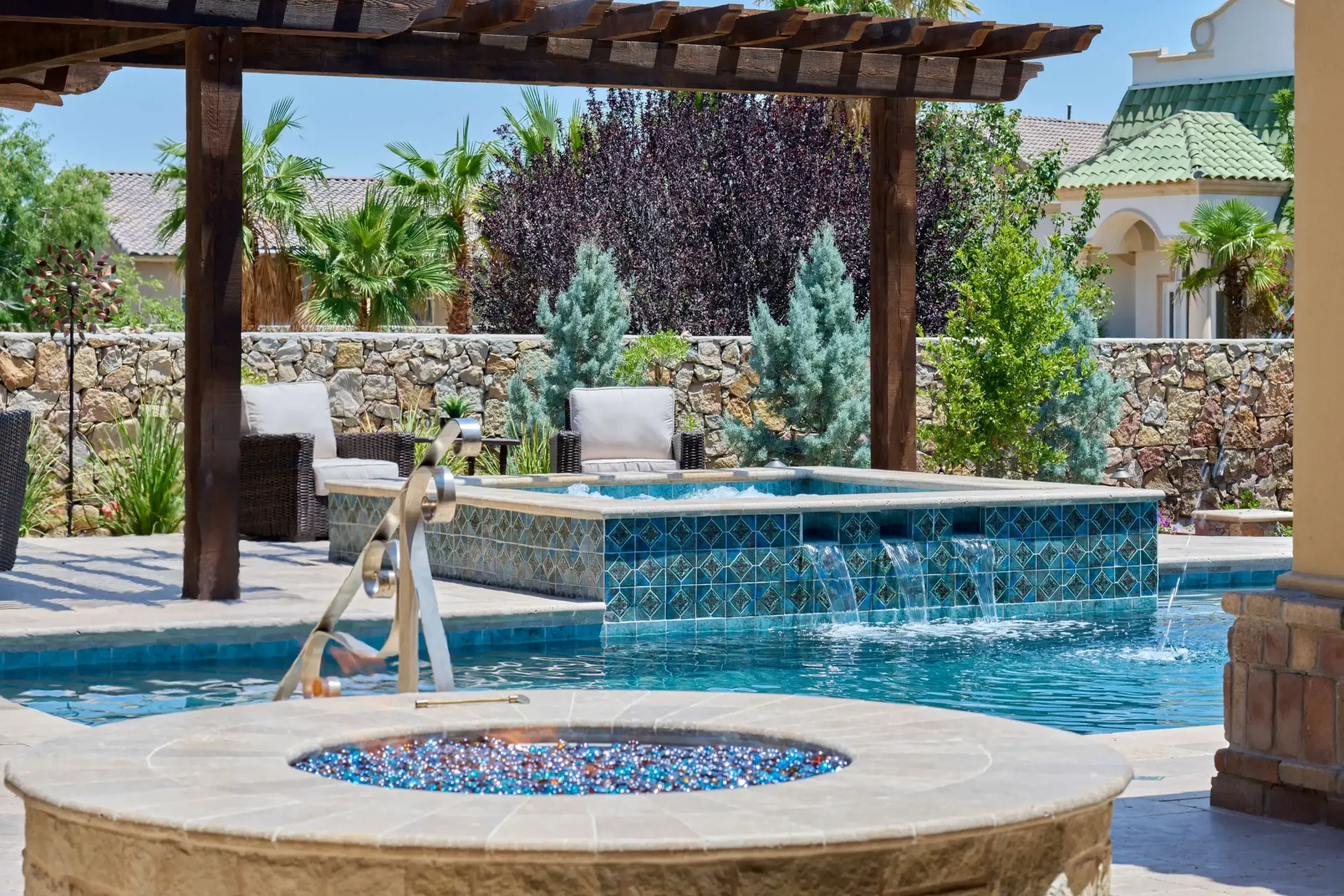 Outdoor pool area with blue water, waterfall, hot tub, fire pit, and pergola.