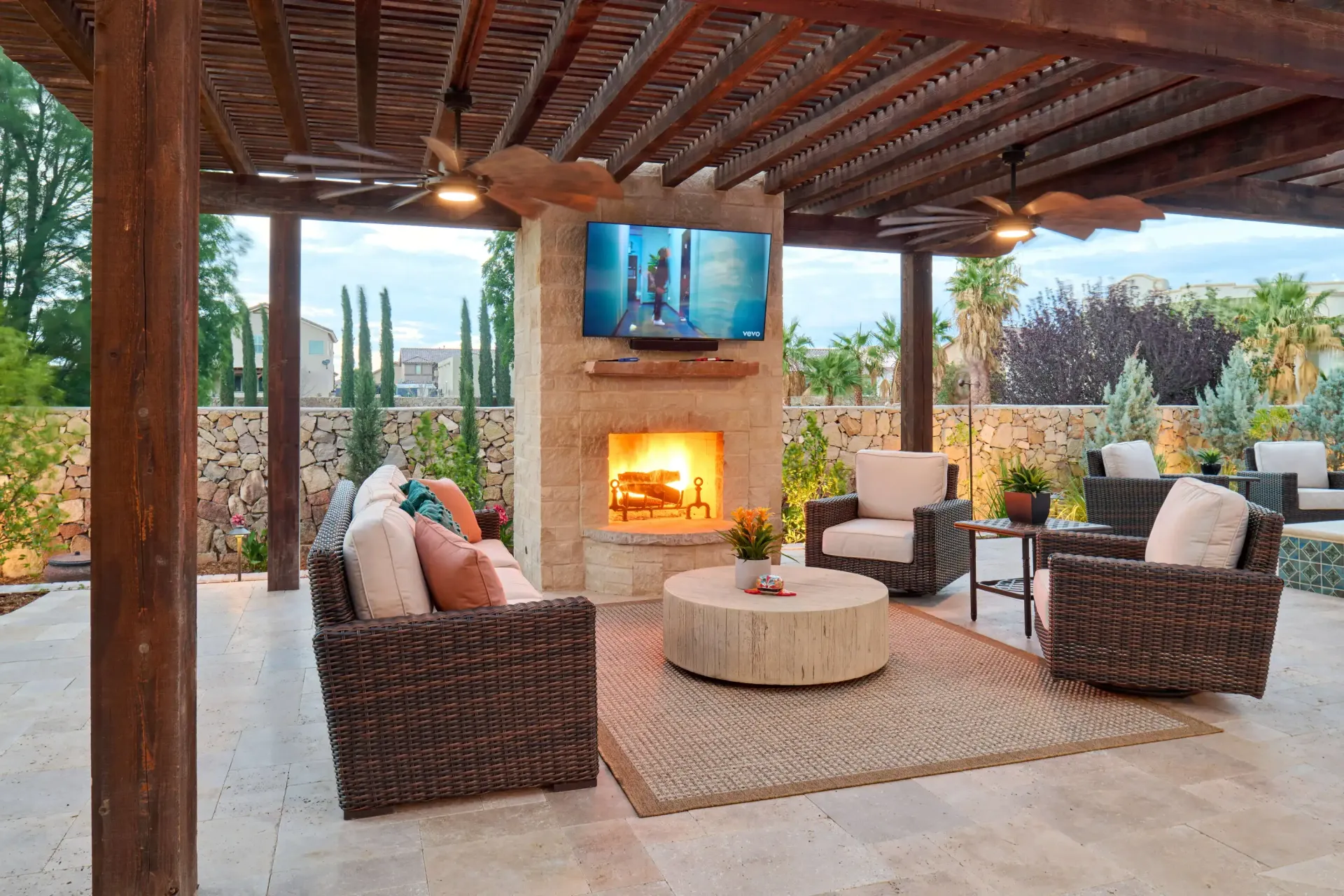 Outdoor living space with fireplace, TV, and seating under a pergola.