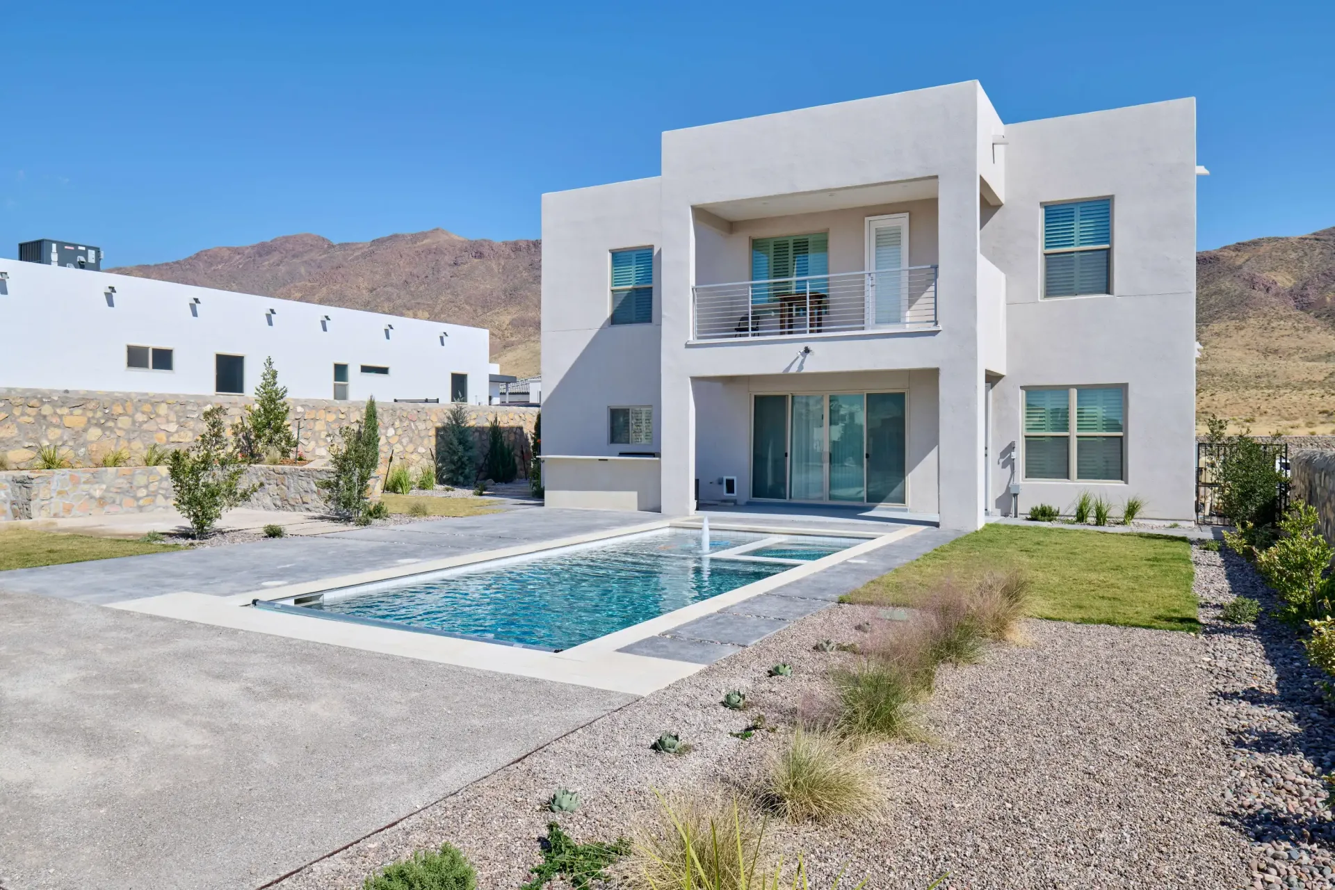 Modern two-story house with a pool in a desert landscape under a clear blue sky.