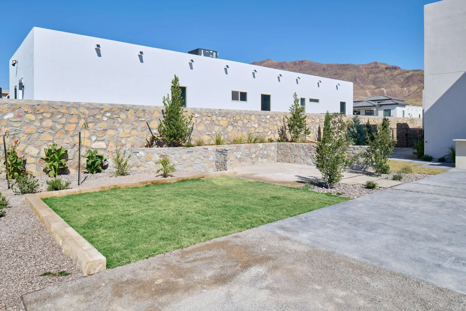 White building with stone wall and small patch of green grass.